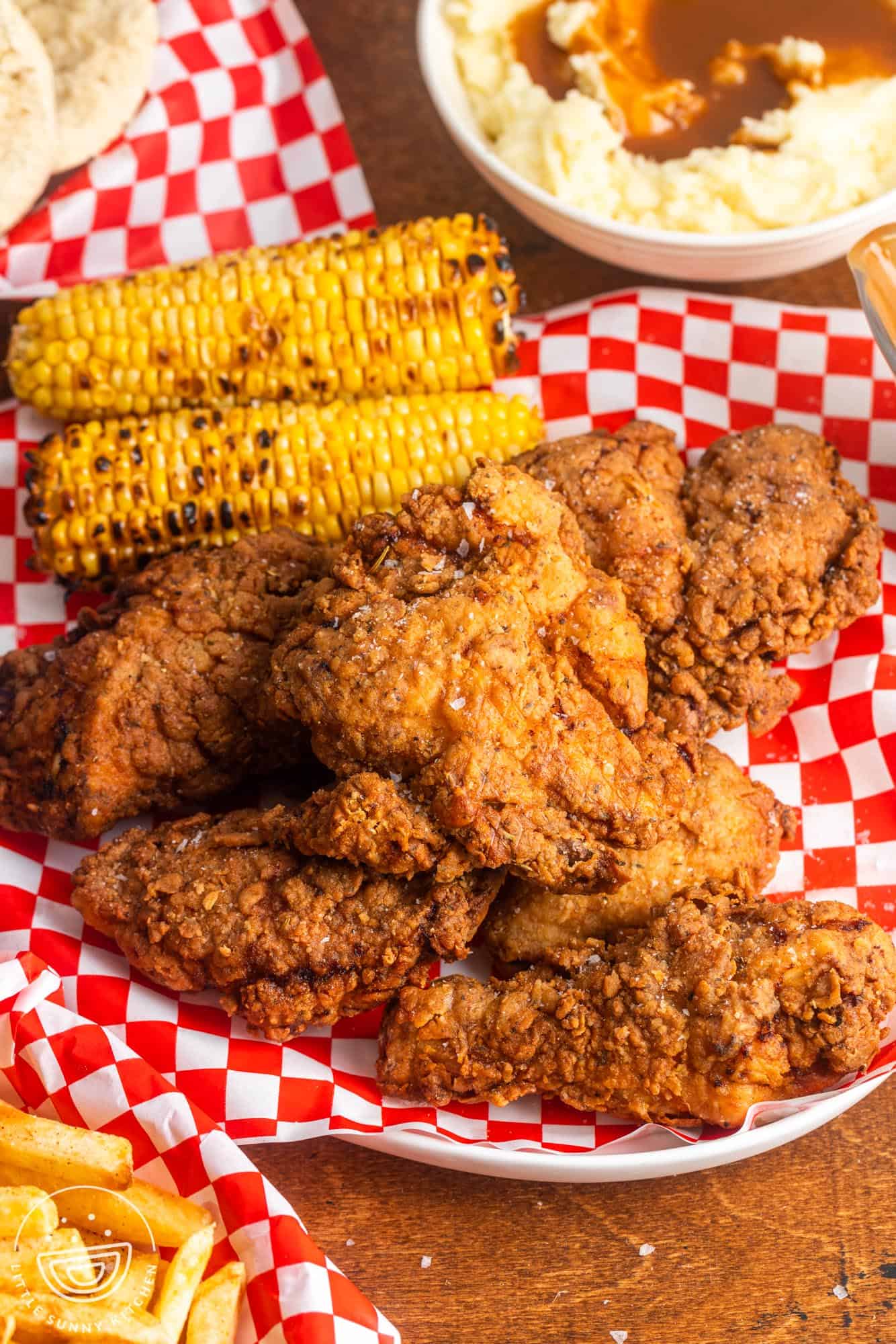 Perfectly Crispy Buttermilk fried chicken on a platter, with grilled corn on the cob in the background