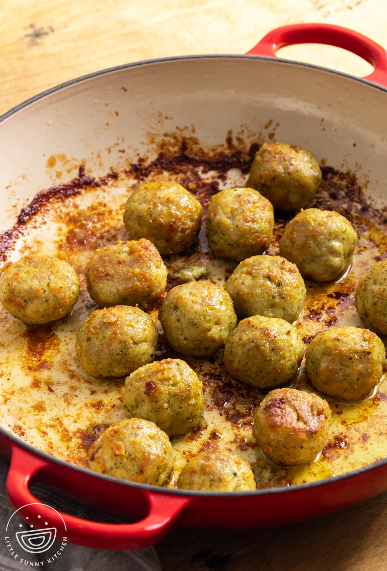 cooked browned chicken pesto meatballs in a pan with oil.