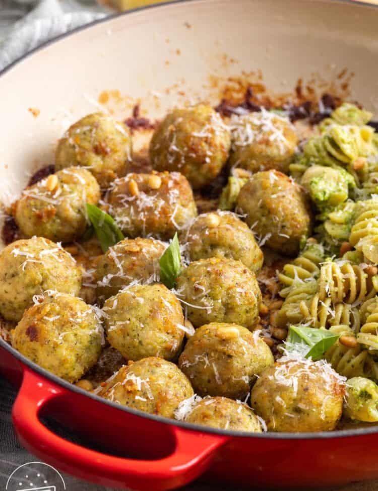 a skillet of chicken meatballs with pesto rotini pasta with pine nuts.