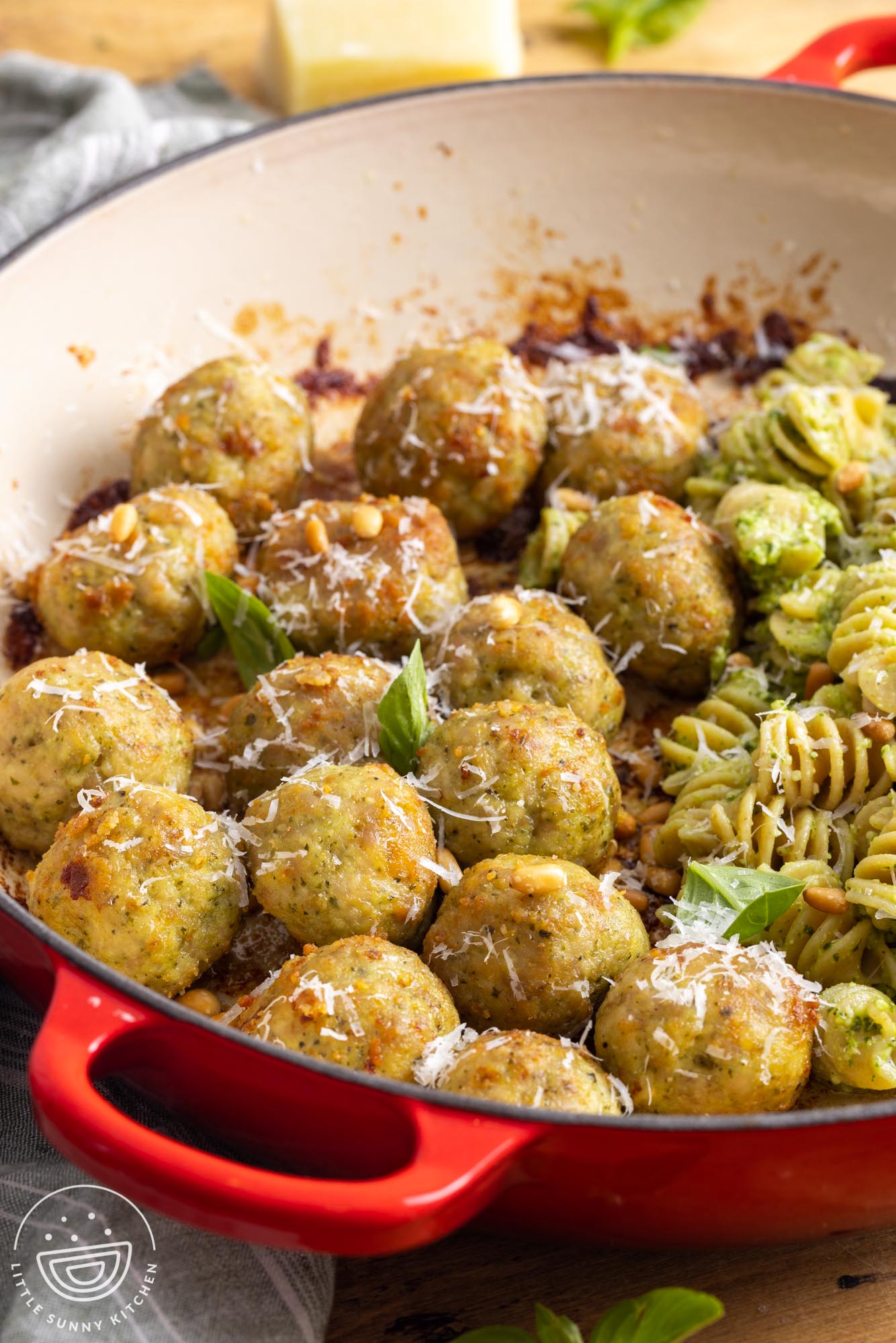 a skillet of chicken meatballs with pesto rotini pasta with pine nuts.