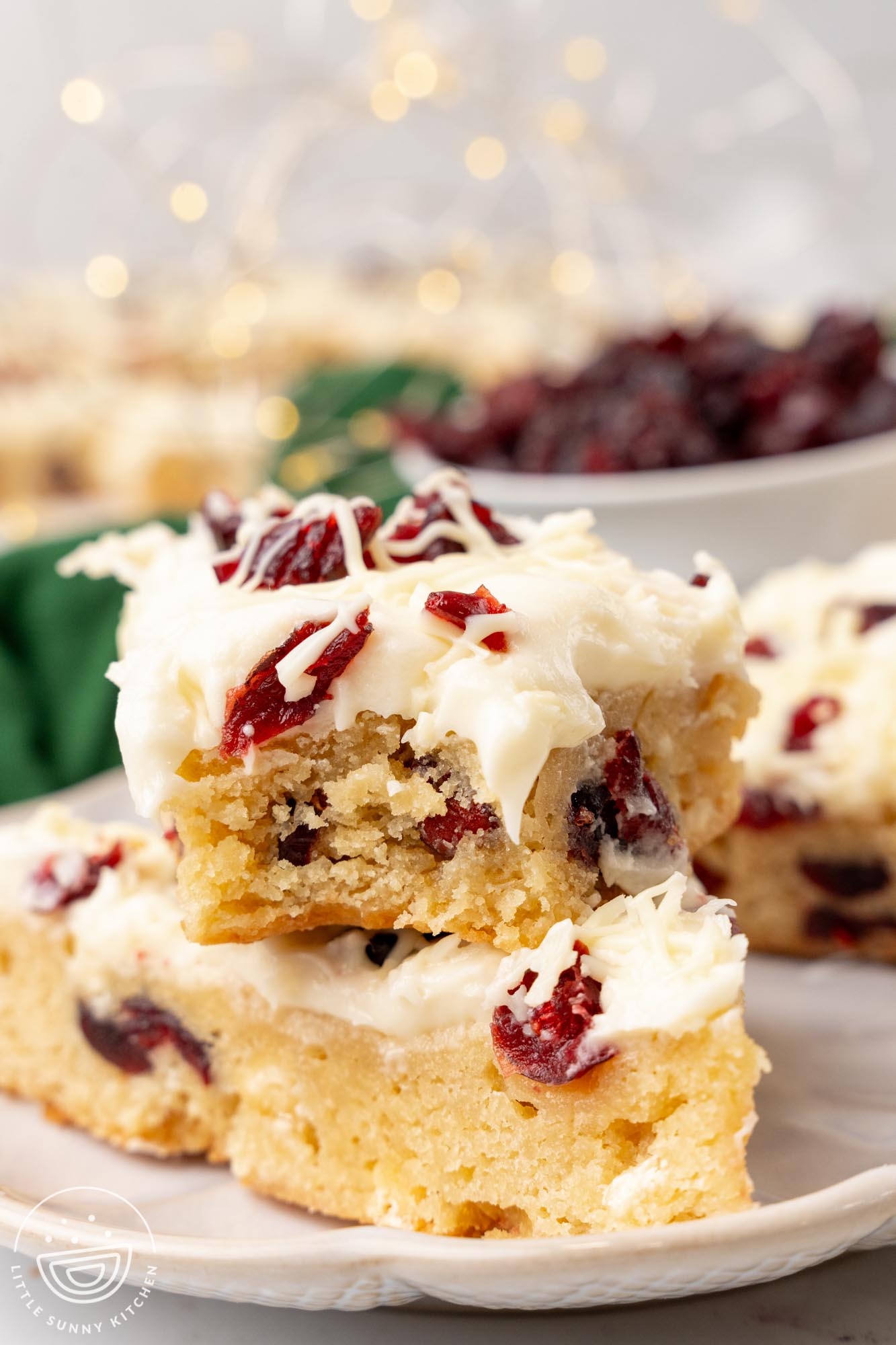 cranberry bliss bars on a plate. One has a bite taken to show the tender, chewy crumb.