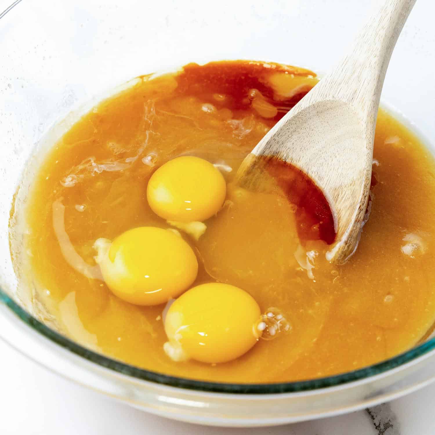 three eggs mixed with melted butter, brown sugar, and vanilla in a glass mixing bowl.