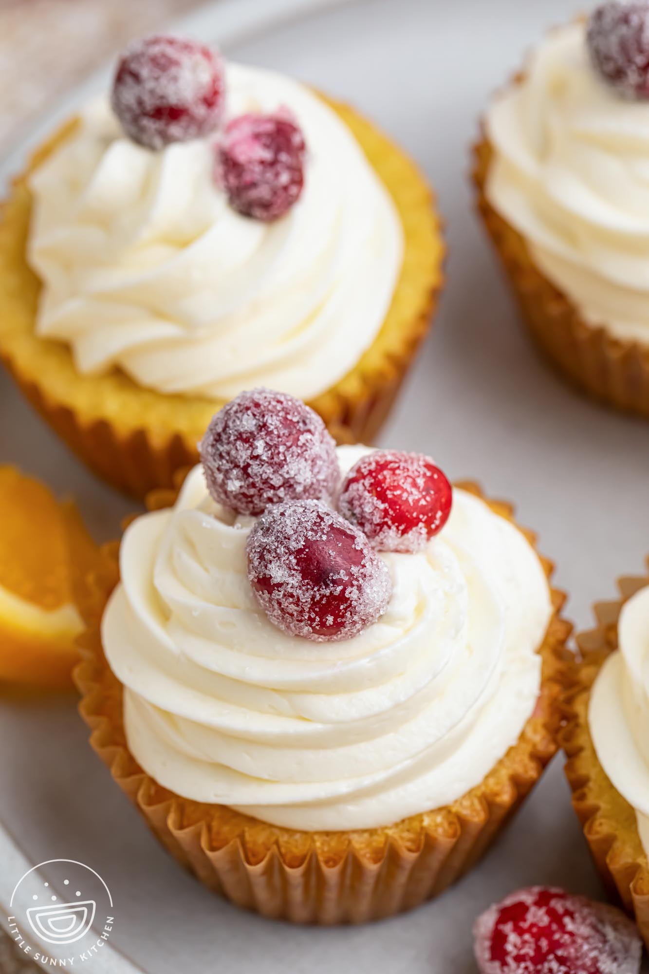 cranberry orange cupcakes, viewed from above. The cupcakes have vanilla frosting swirls and sugared cranberries on top.