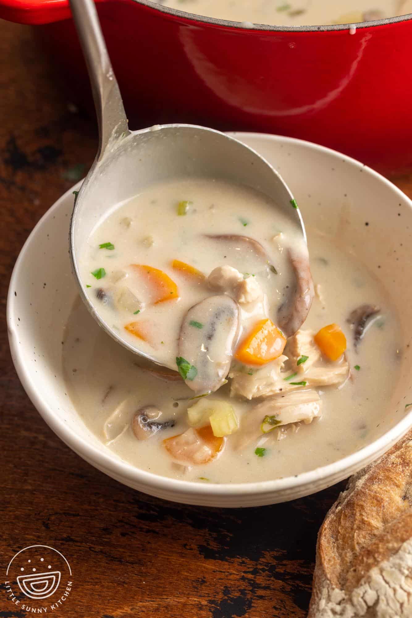 a ladle serving creamy mushroom chicken soup into a soup bowl.