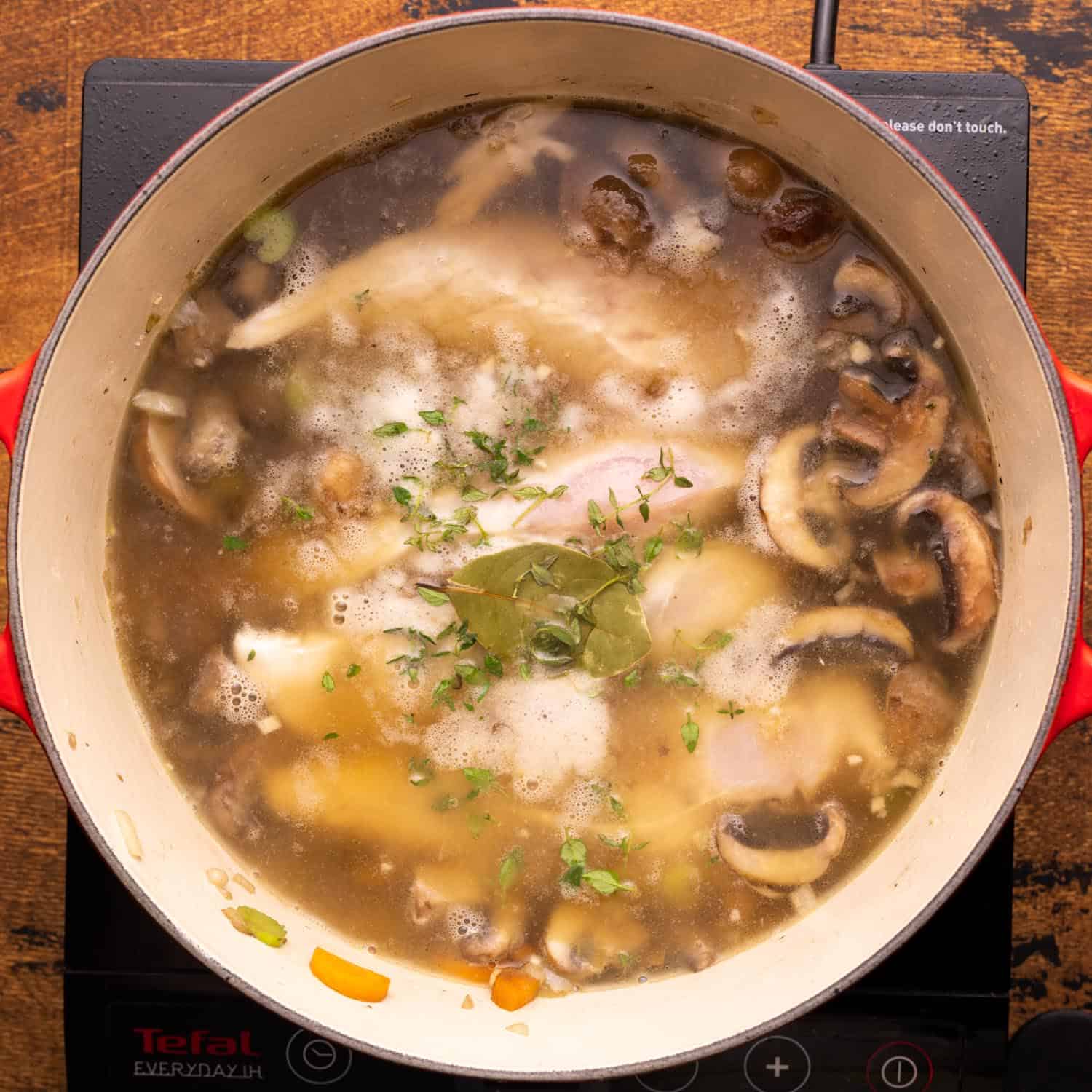 broth, chicken, and herbs added to sauteed veggies in a soup pot.