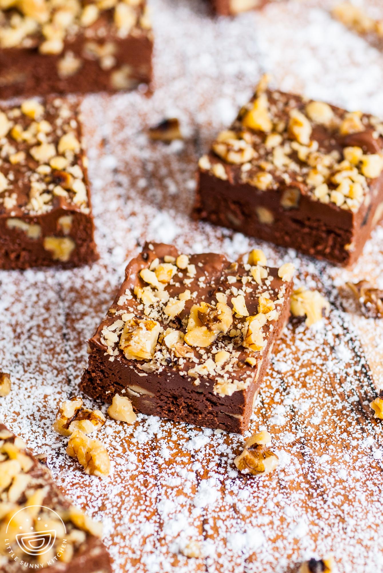 fantasy fudge squares with walnuts on a board sprinkled with powdered sugar.