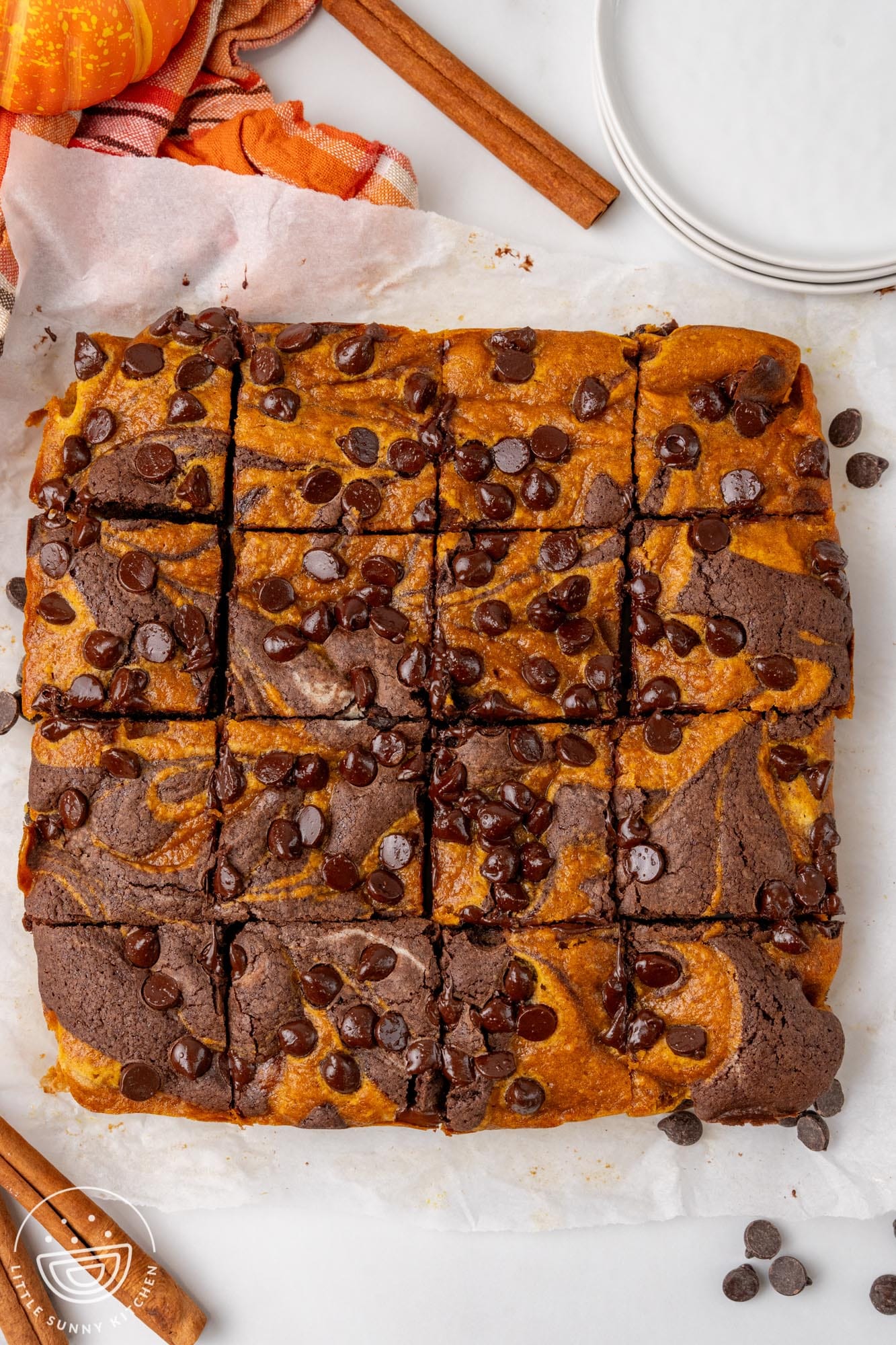 a square pan of pumpkin brownies, baked, on parchment paper, cut into 16 square pieces.