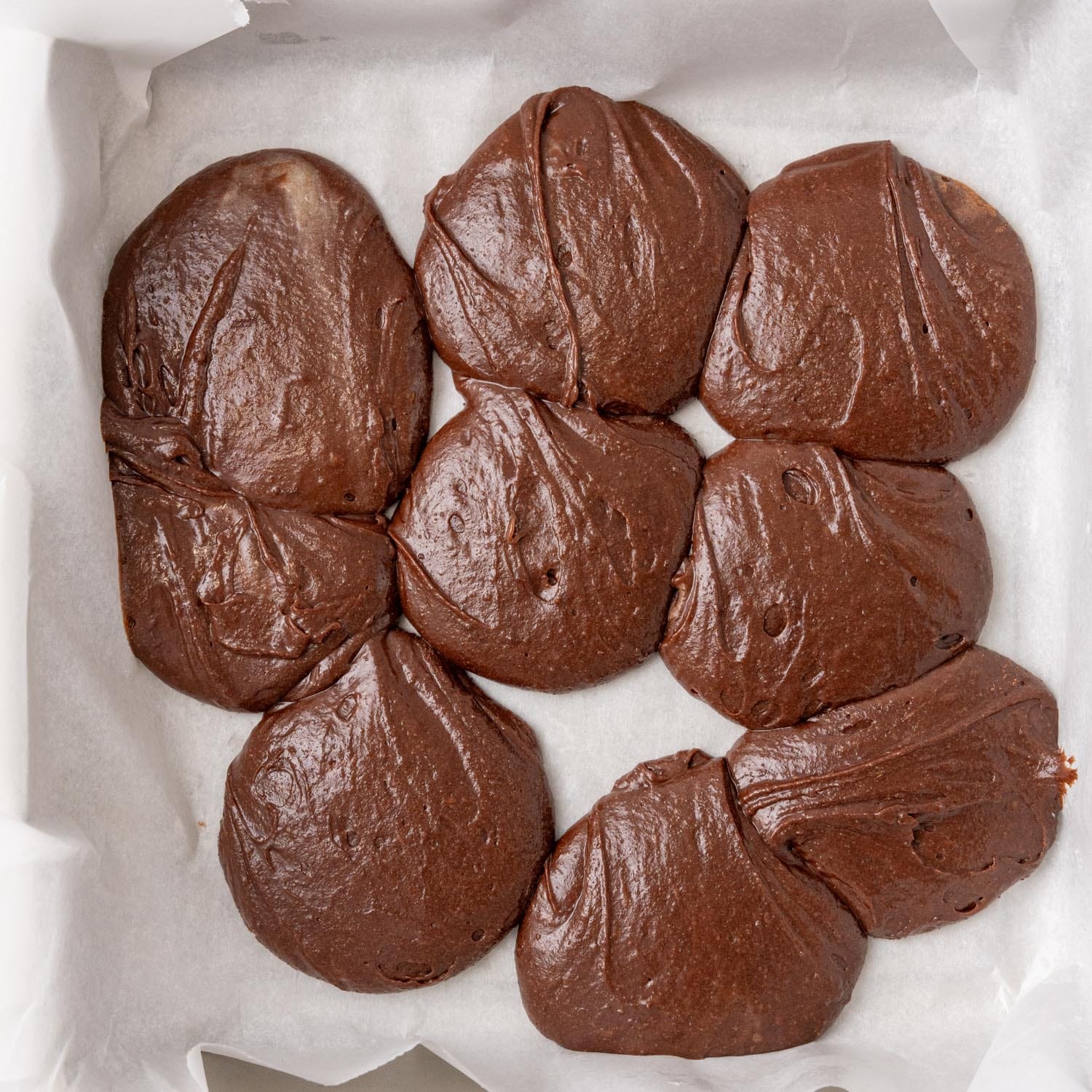 dollops of brownie batter in a parchment lined baking pan.