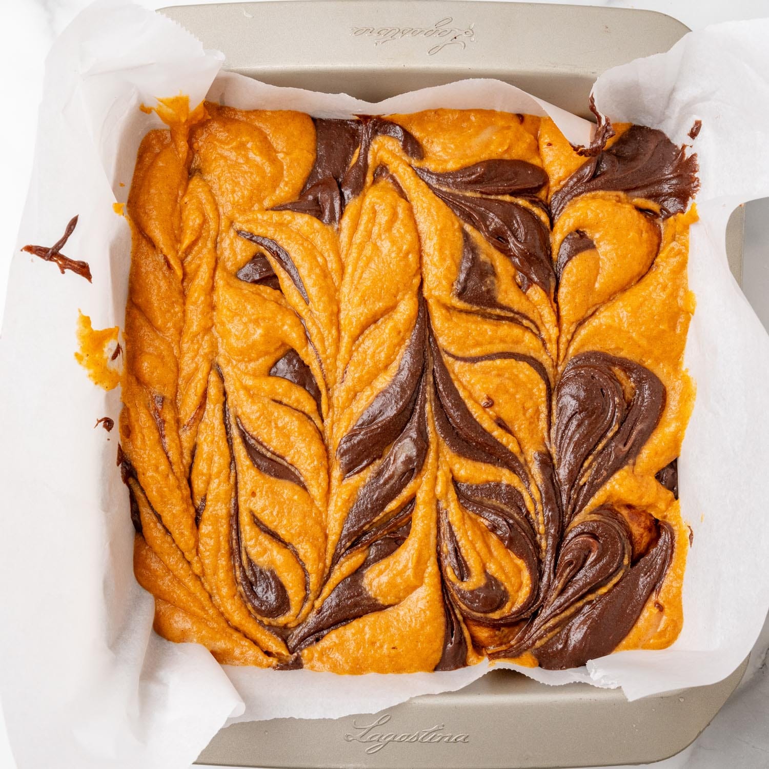 pumpkin and chocolate brownie batter in a pan, swirled.