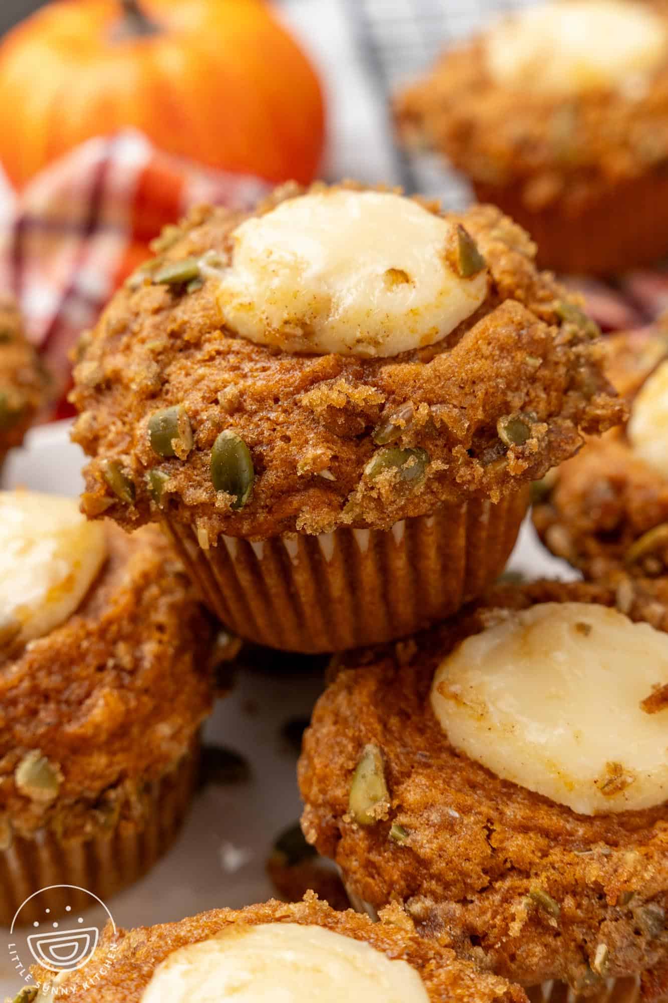 a stack of pumpkin cream cheese muffins topped with raw pumpkin seeds, brown sugar and cream cheese filling.