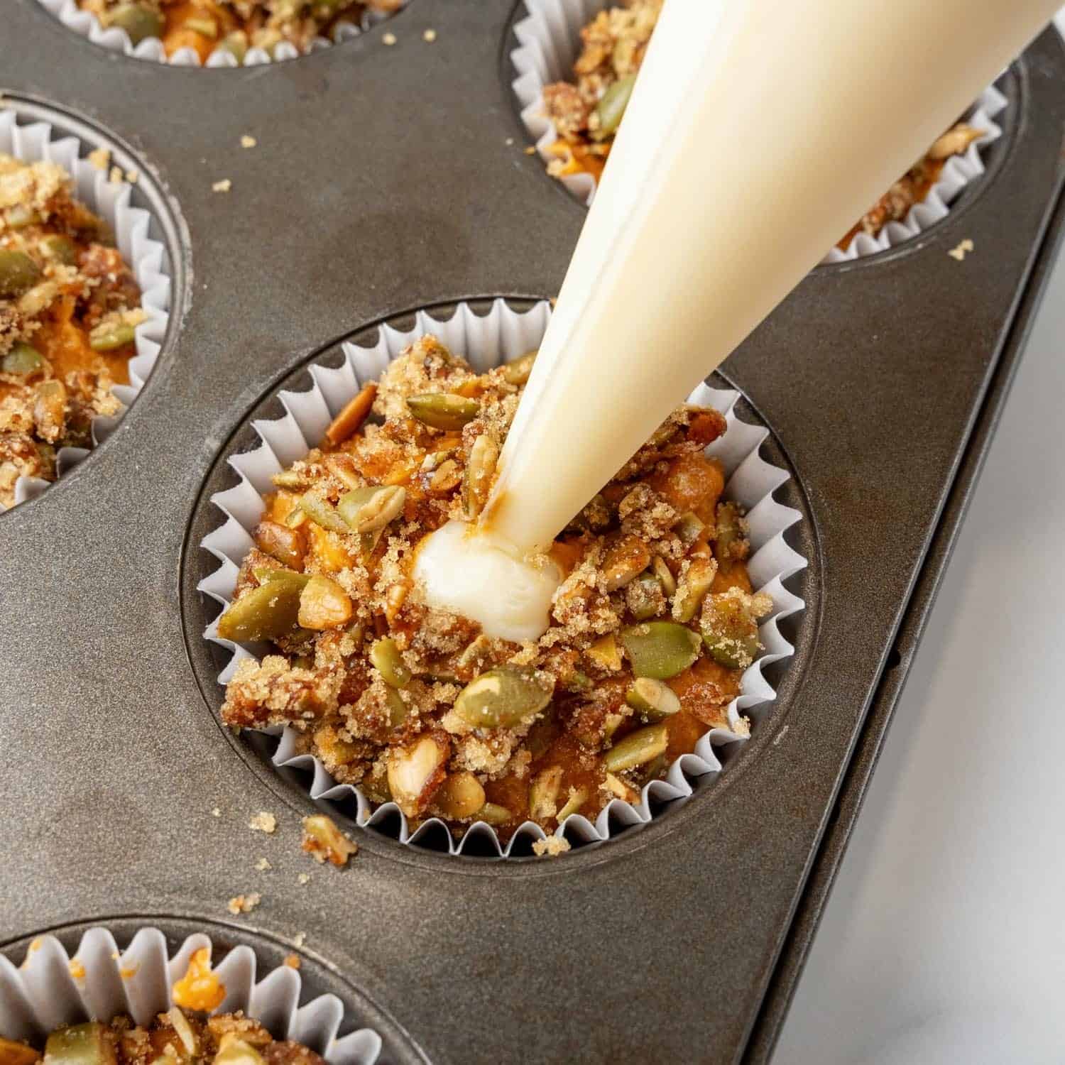 a disposable piping bag adding cream cheese filling to pumpkin muffins before they are baked.