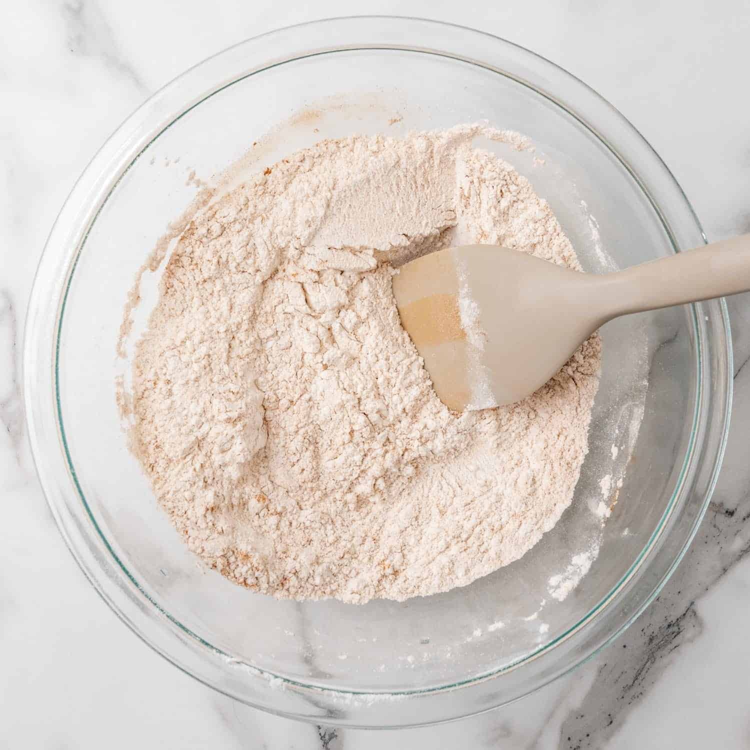 flour stirred in a glass mixing bowl with a gray spatula.