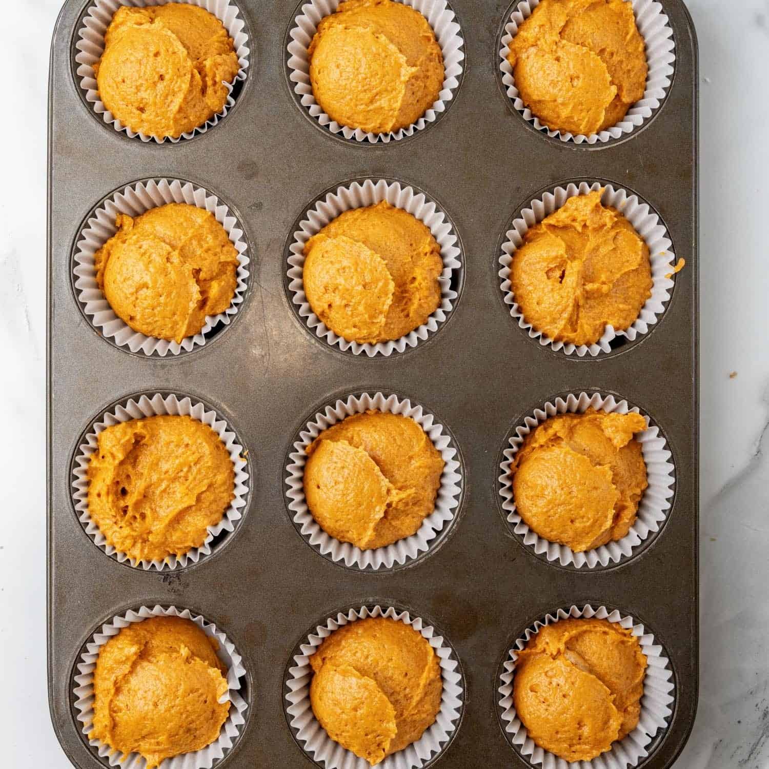 pumpkin muffin batter scooped into paper liners in a cupcake tin.