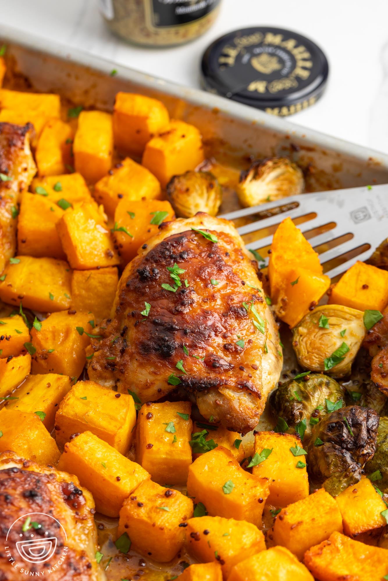 a metal spatula lifting a chicken thigh from a sheet pan filled with roasted vegetables.