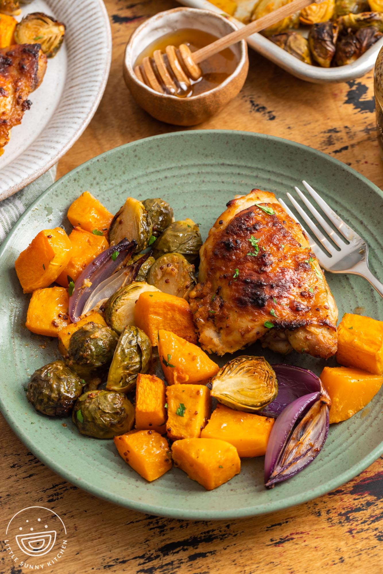 a green plate holding a serving of sheet pan honey mustard chicken thighs and veggies.