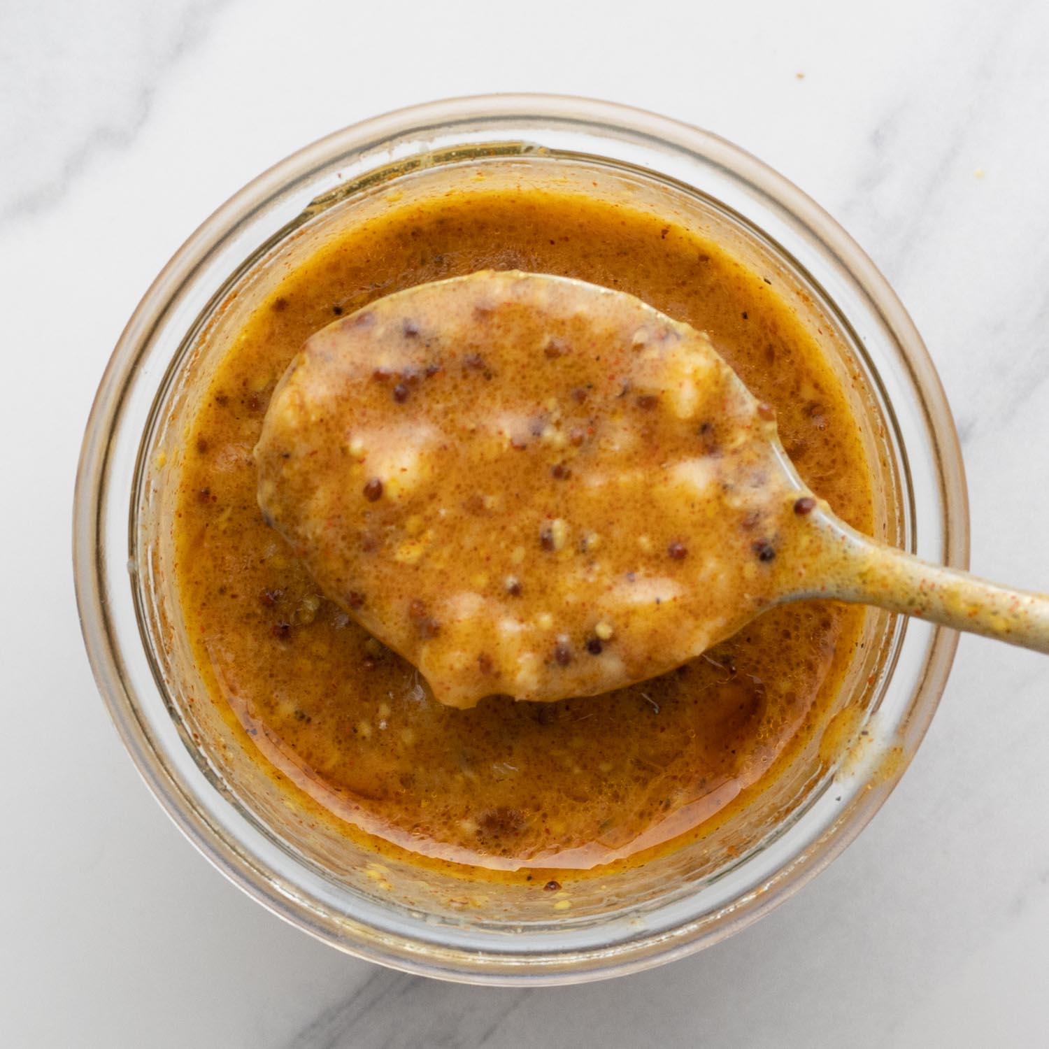 honey mustard sauce for chicken thighs in a jar, held up with a spoon to show the texture.