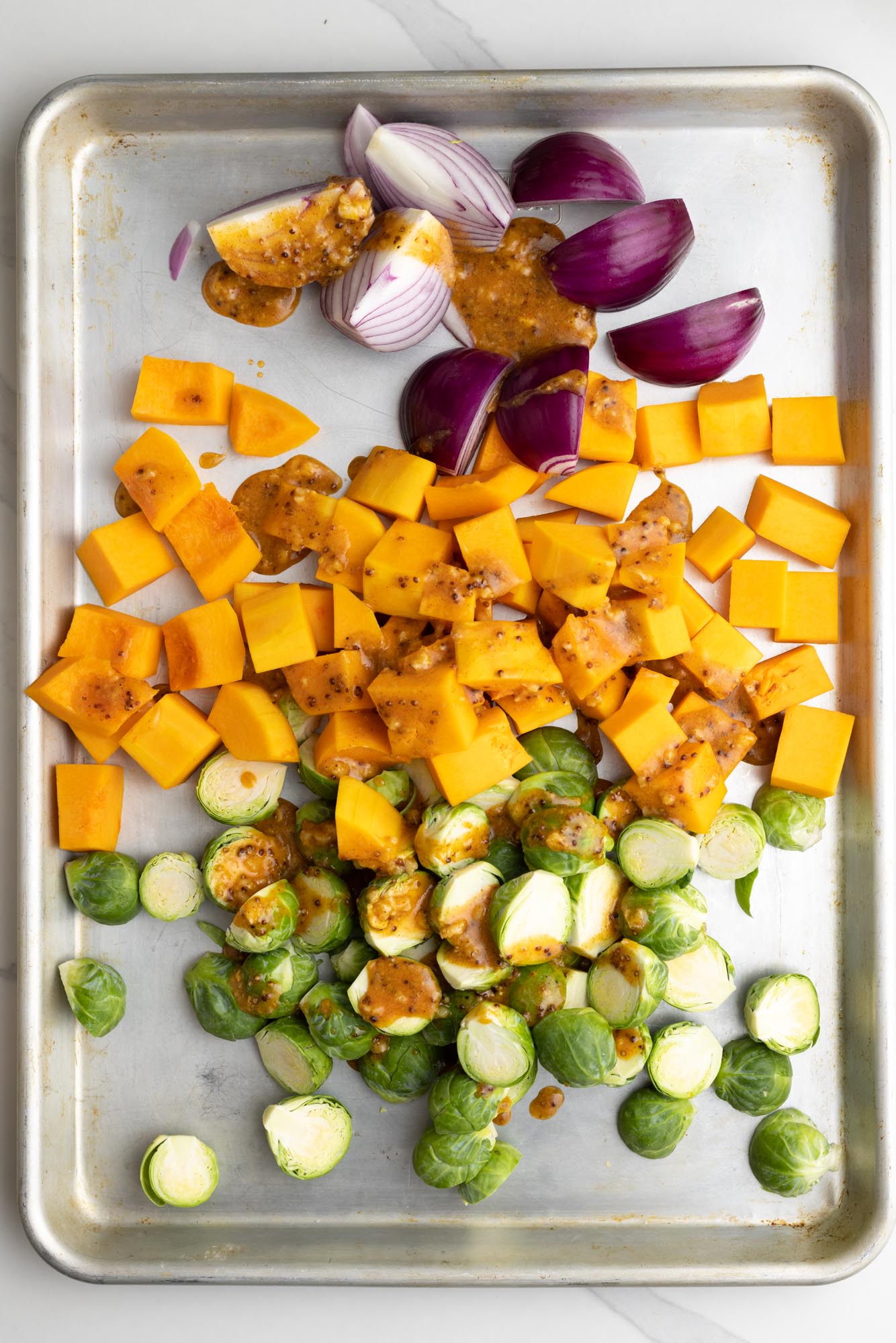 quartered red onion, diced butternut squash, and halved brussels sprouts, raw, on a sheet pan, drizzled in homemade honey mustard sauce.