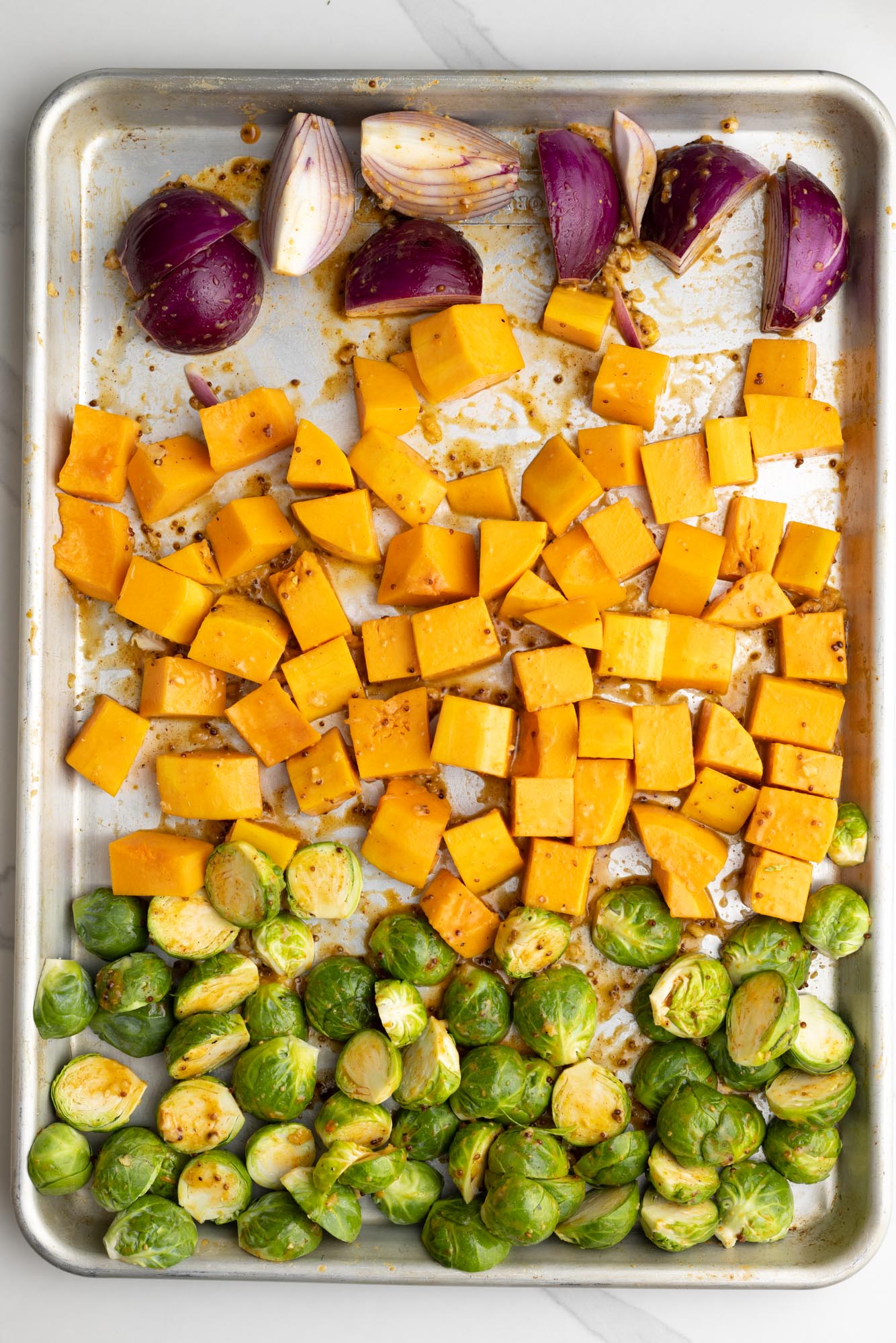 brussel sprouts, squash, and onions with sauce, arranged on a sheet pan in separate sections.