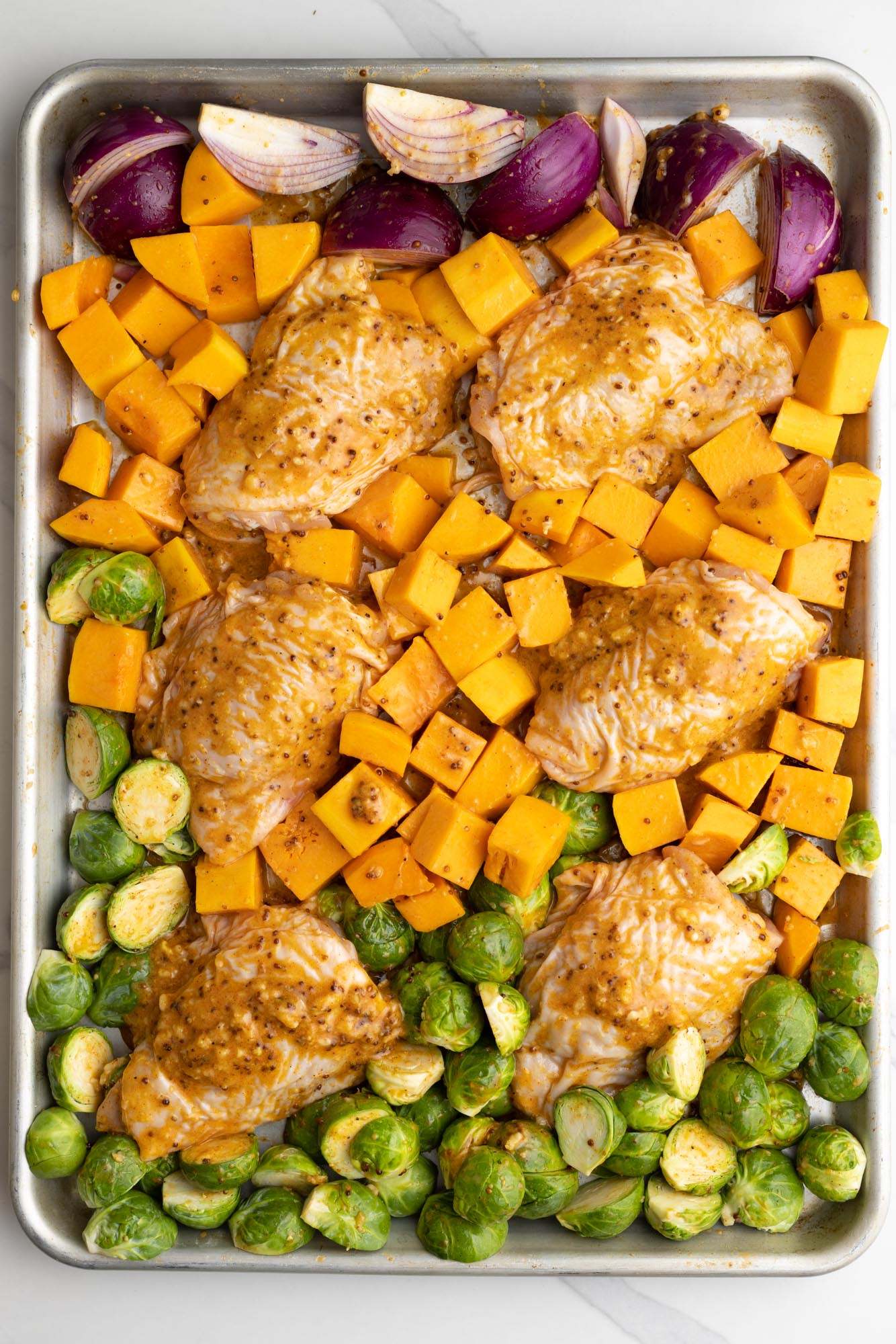 chicken thighs nestled into veggies on a sheet pan.