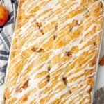 apple slab pie with icing drizzled over it, on a counter with a blue and white striped towel.