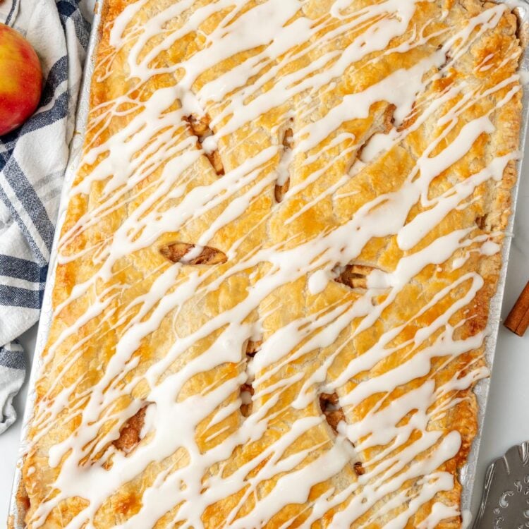 apple slab pie with icing drizzled over it, on a counter with a blue and white striped towel.