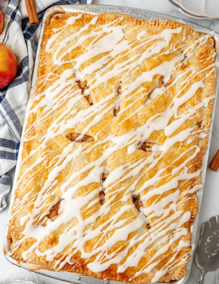 apple slab pie with icing drizzled over it, on a counter with a blue and white striped towel.