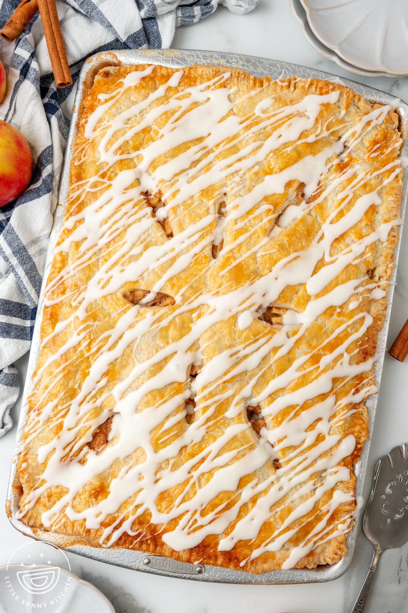 apple slab pie with icing drizzled over it, on a counter with a blue and white striped towel.