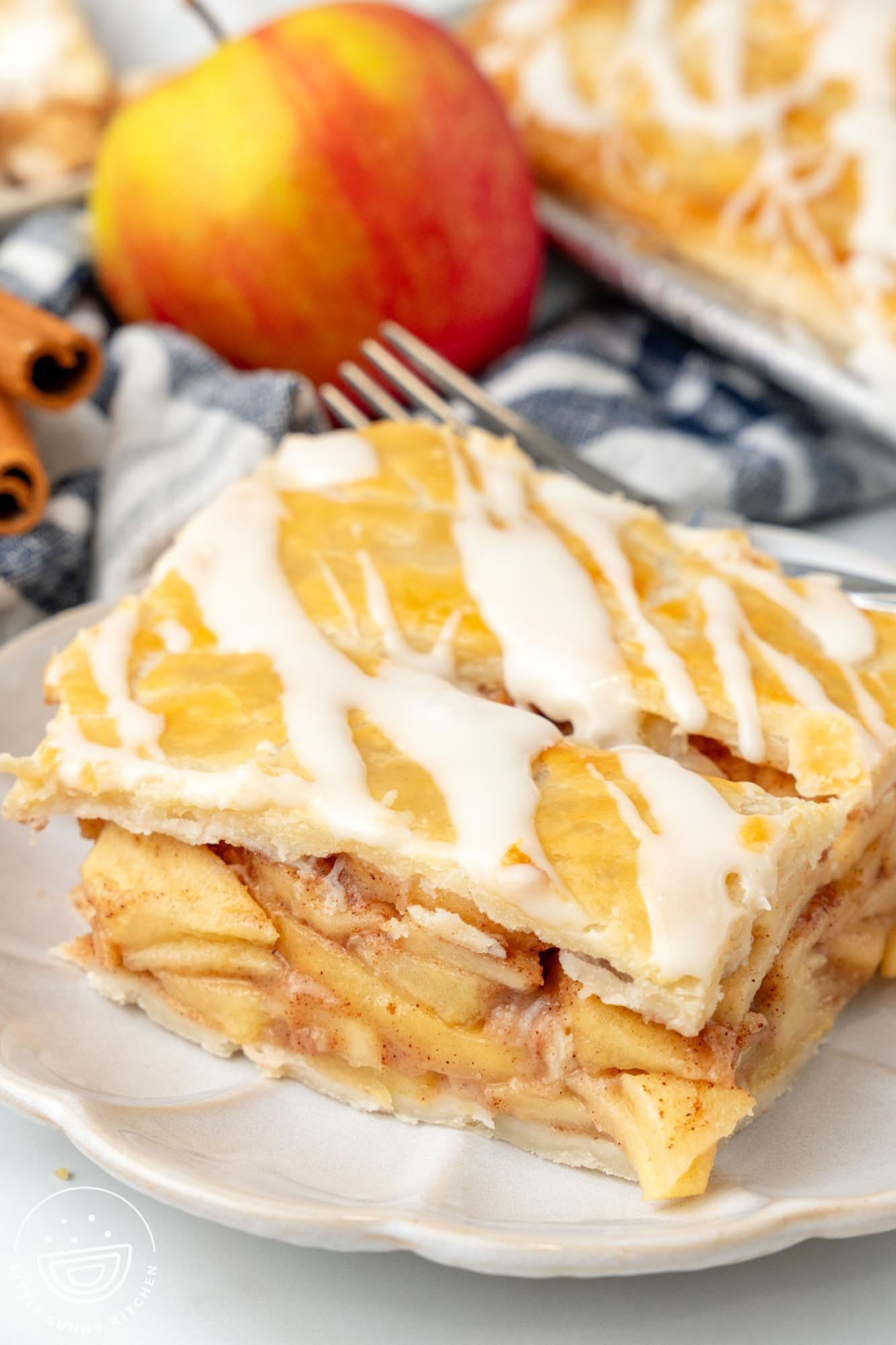 a plate holding a square piece of apple slab pie. In the background is a whole apple.