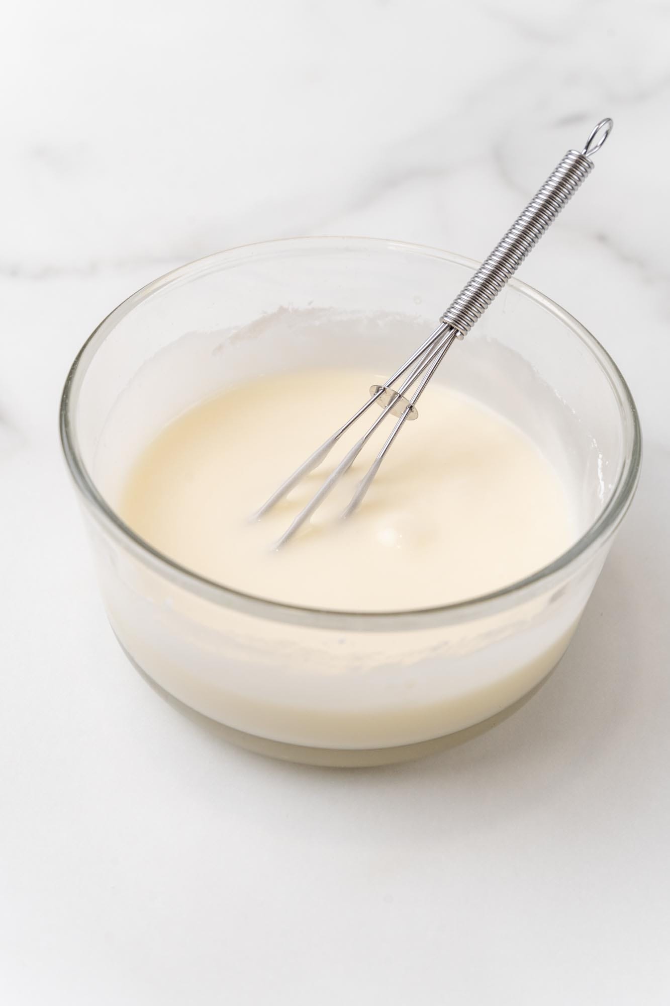 icing mixed with a small whisk in a glass bowl.