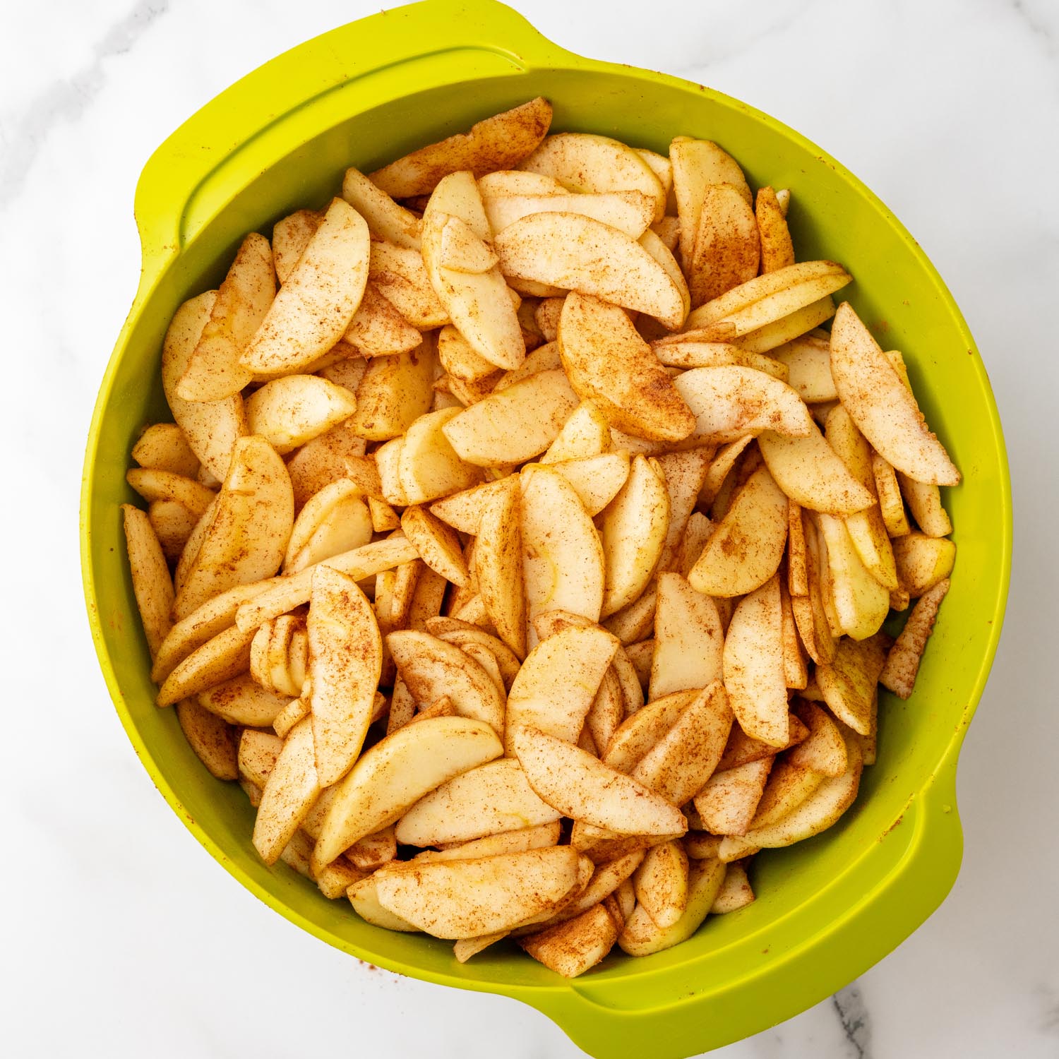 cinnamon sugar apple slices in a green mixing bowl.