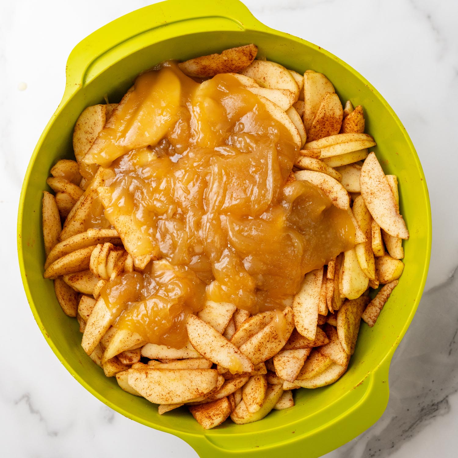 caramel sauce poured over sliced apples in a green mixing bowl.