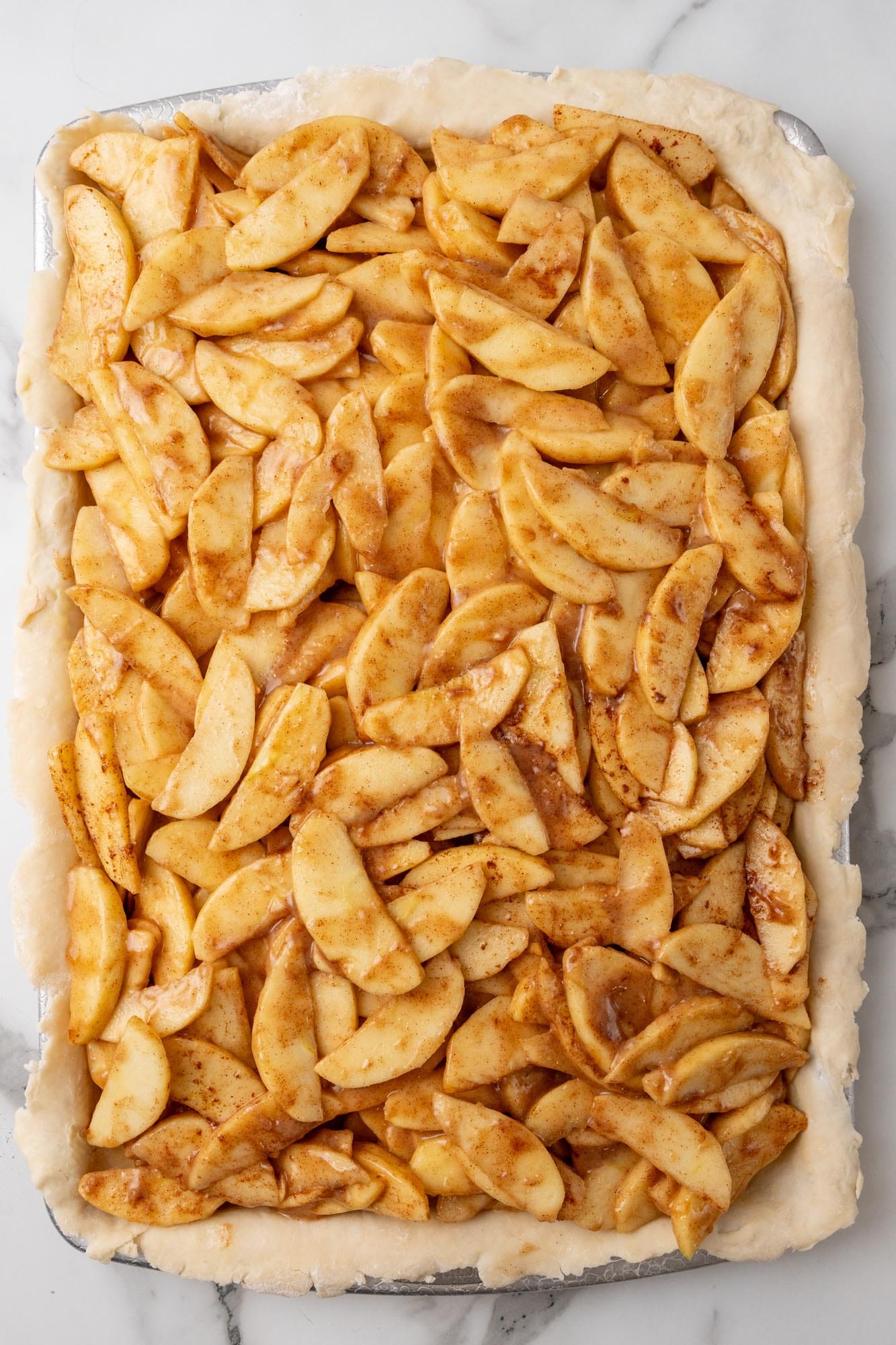 apple pie filling added to a pie crust on a sheet pan to make slab pie.