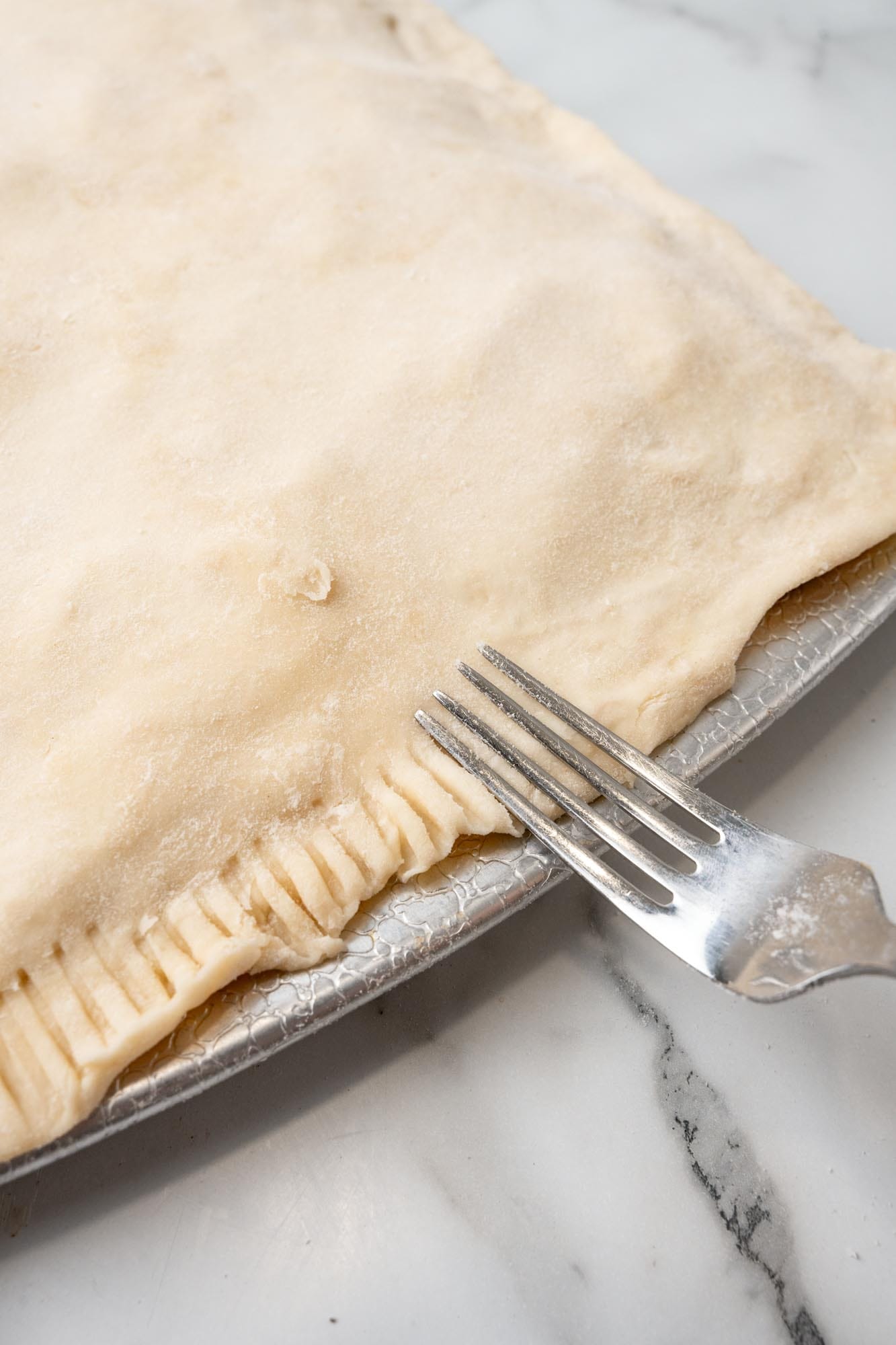 a fork pressing down the edges of dough around an apple slab pie.