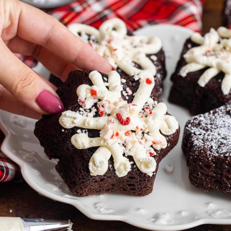 crushed peppermints and holiday sprinkles on top of chocolate mini cakes with white frosting. A hand is holding one up.