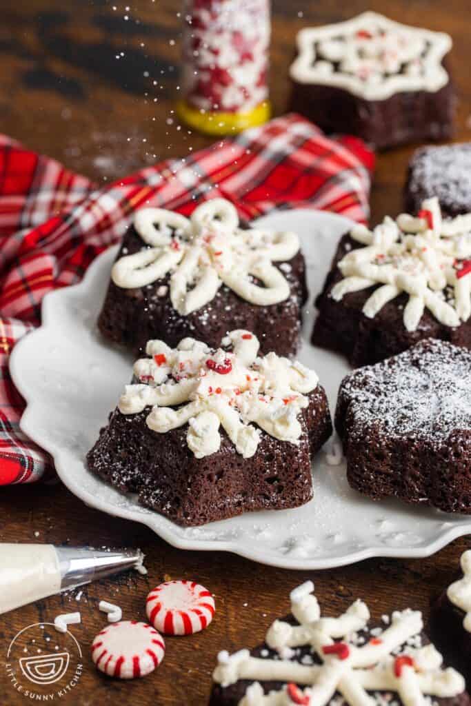a white plate of chocolate peppermint mini cakes. Powdered sugar is being sprinkled over them.