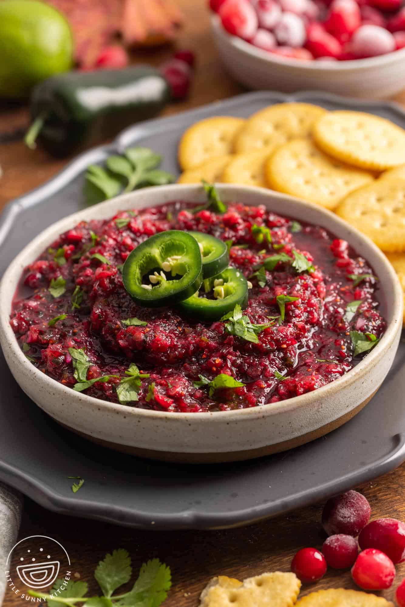 a bowl of cranberry salsa with jalapeno slices on top, next to a pile of buttery crackers.