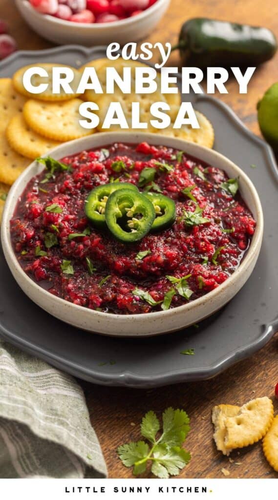 a ceramic bowl of cranberry salsa with jalapeno slices on a tray with ritz crackers.