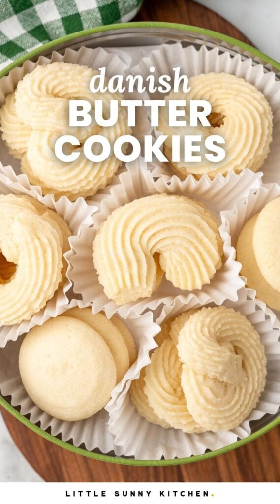 a green tin holding danish butter cookies in white paper liners. The cookies are in various shapes like pretzels, crescents, and circles.