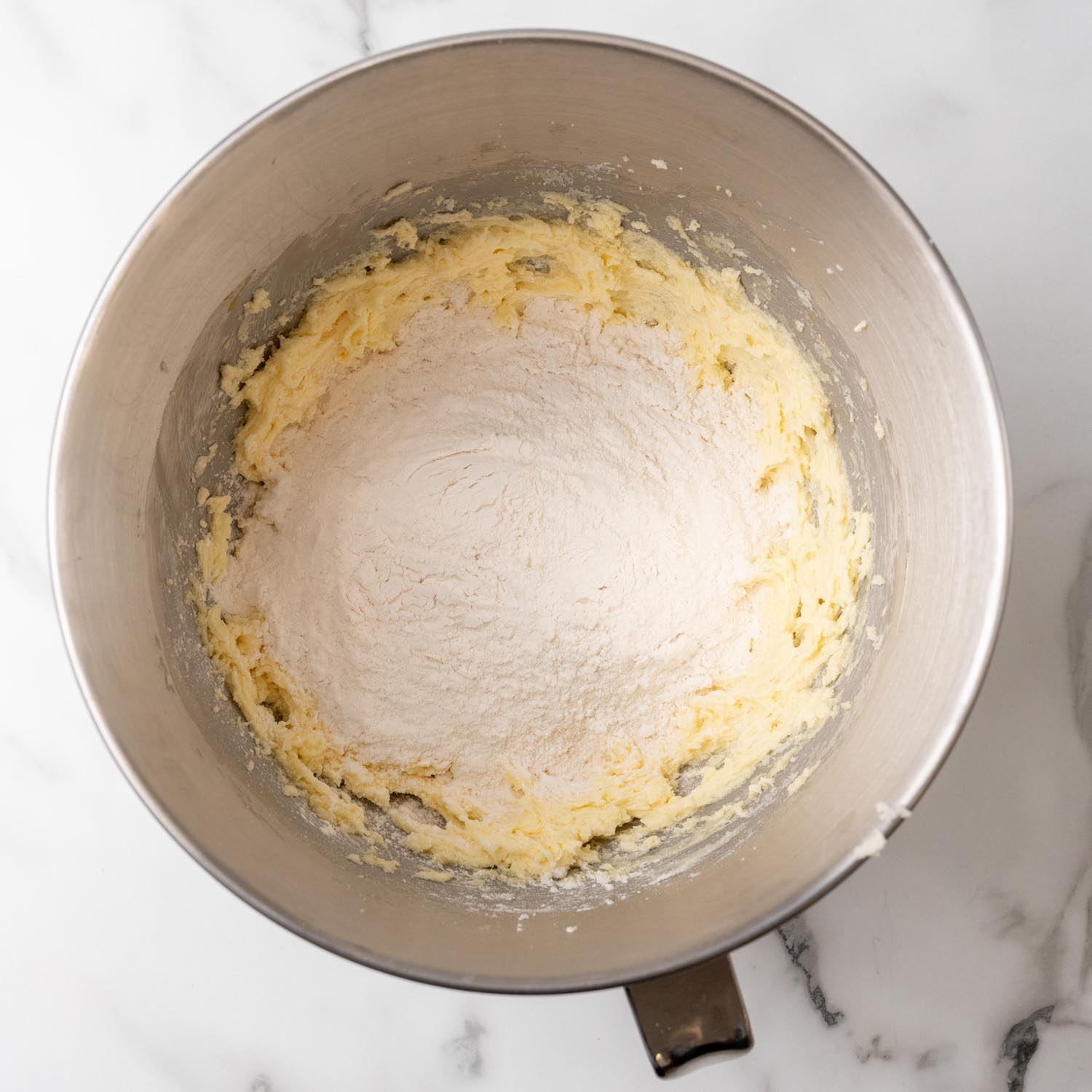 flour added to butter mixture to make cookie dough in a metal mixing bowl.