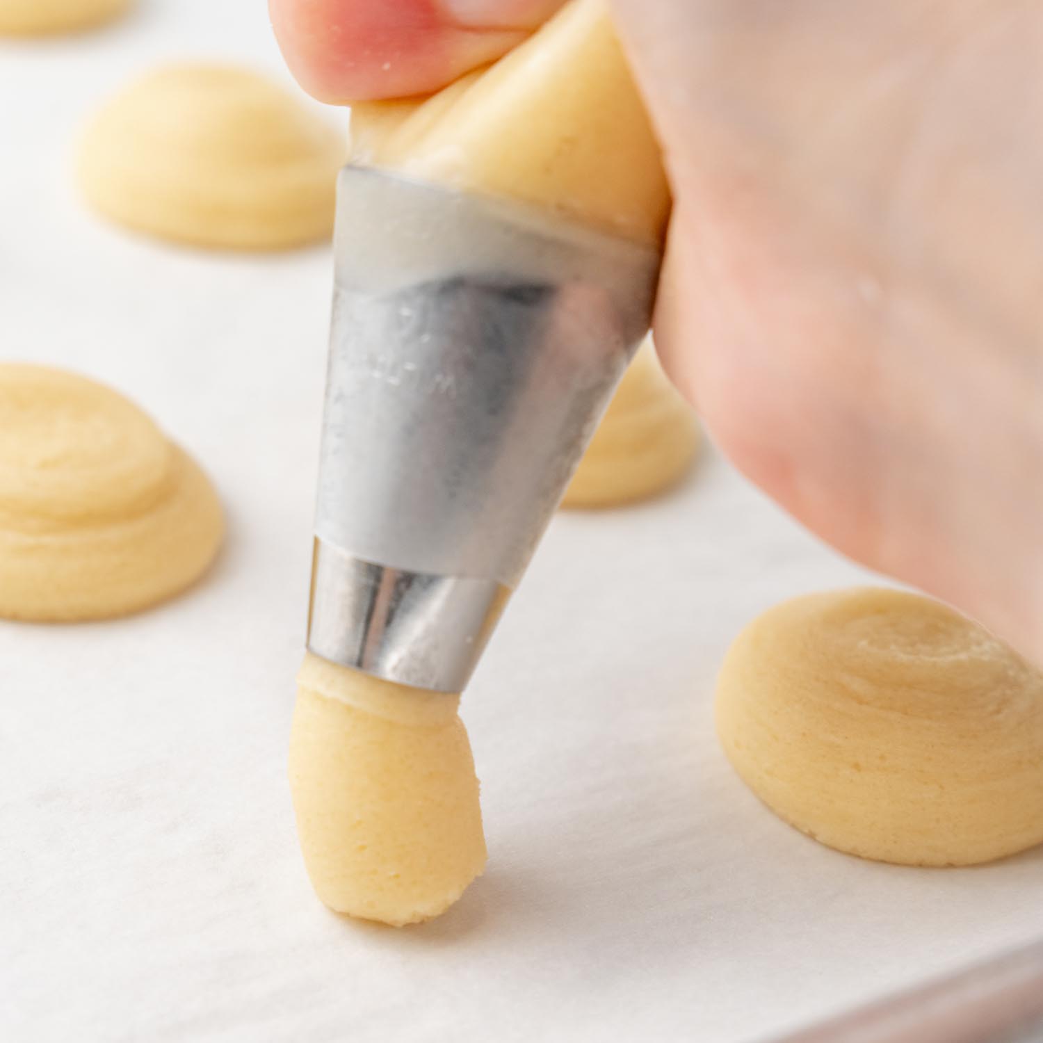 a hand using a piping bag with a large round tip to pipe circular cookies.