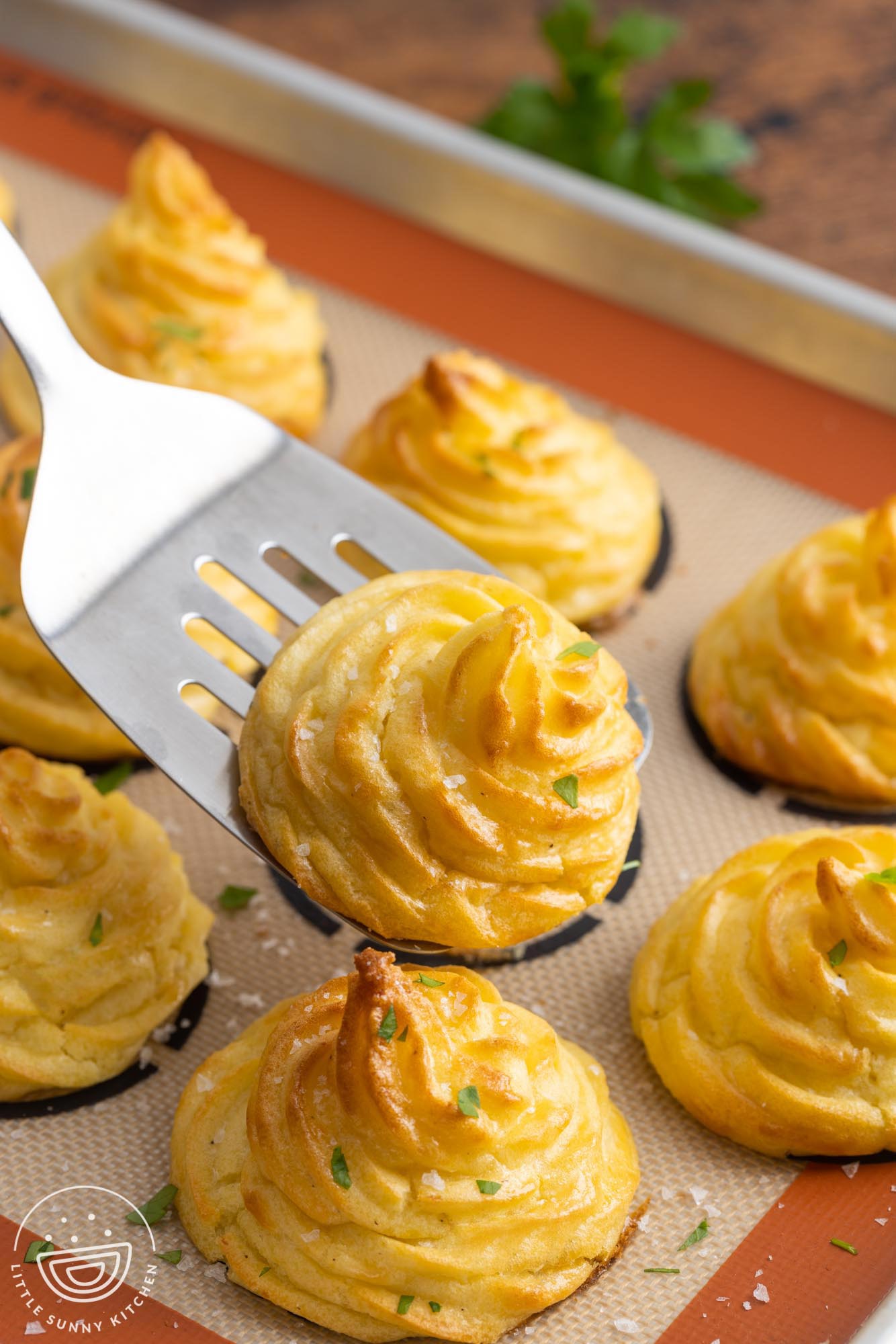 duchess potatoes baked on a silpat mat, one is lifted up with a metal spatula. 