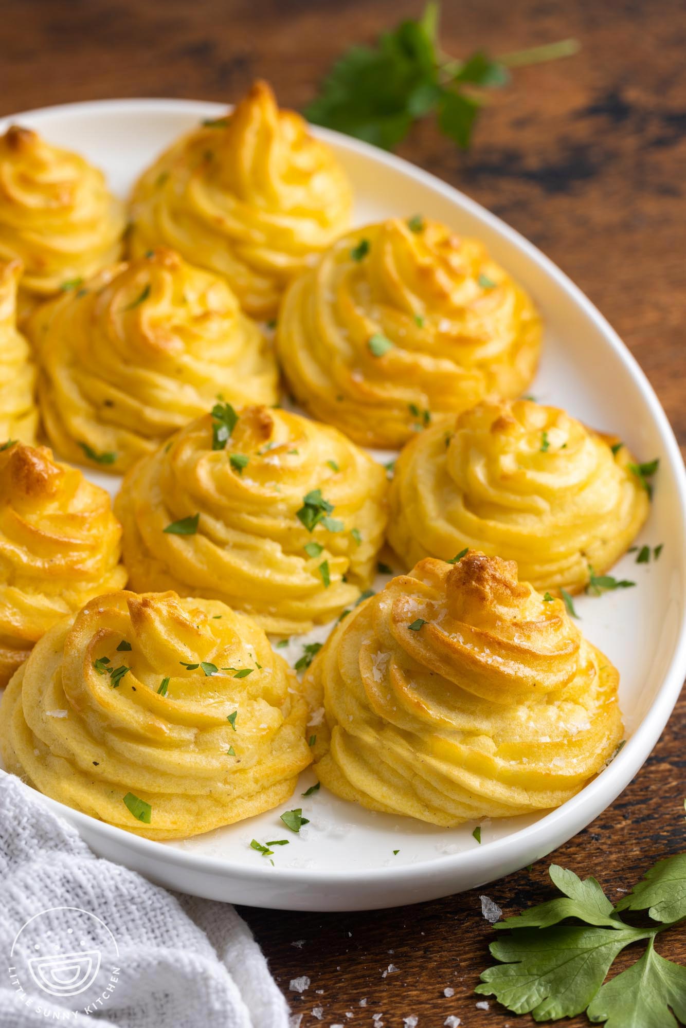 an oval platter of duchess potato swirls garnished with chopped parsley. 