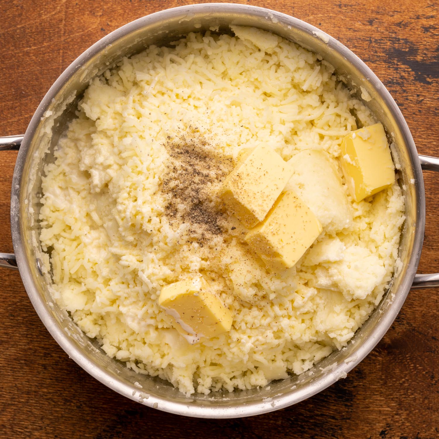 butter, cream, and seasonings added to riced potatoes in a metal pot.