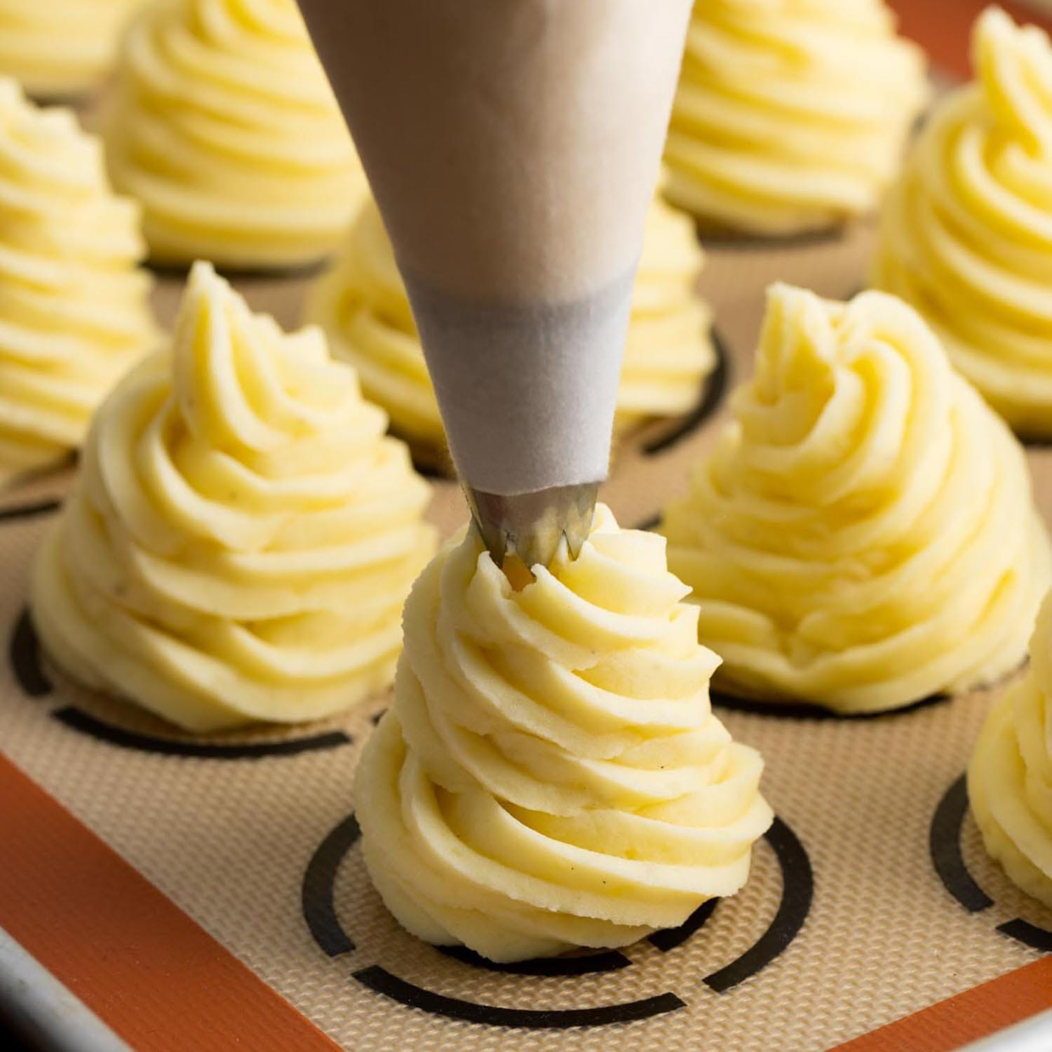 a piping bag creating swirls of mashed potatoes on a silpat mat.