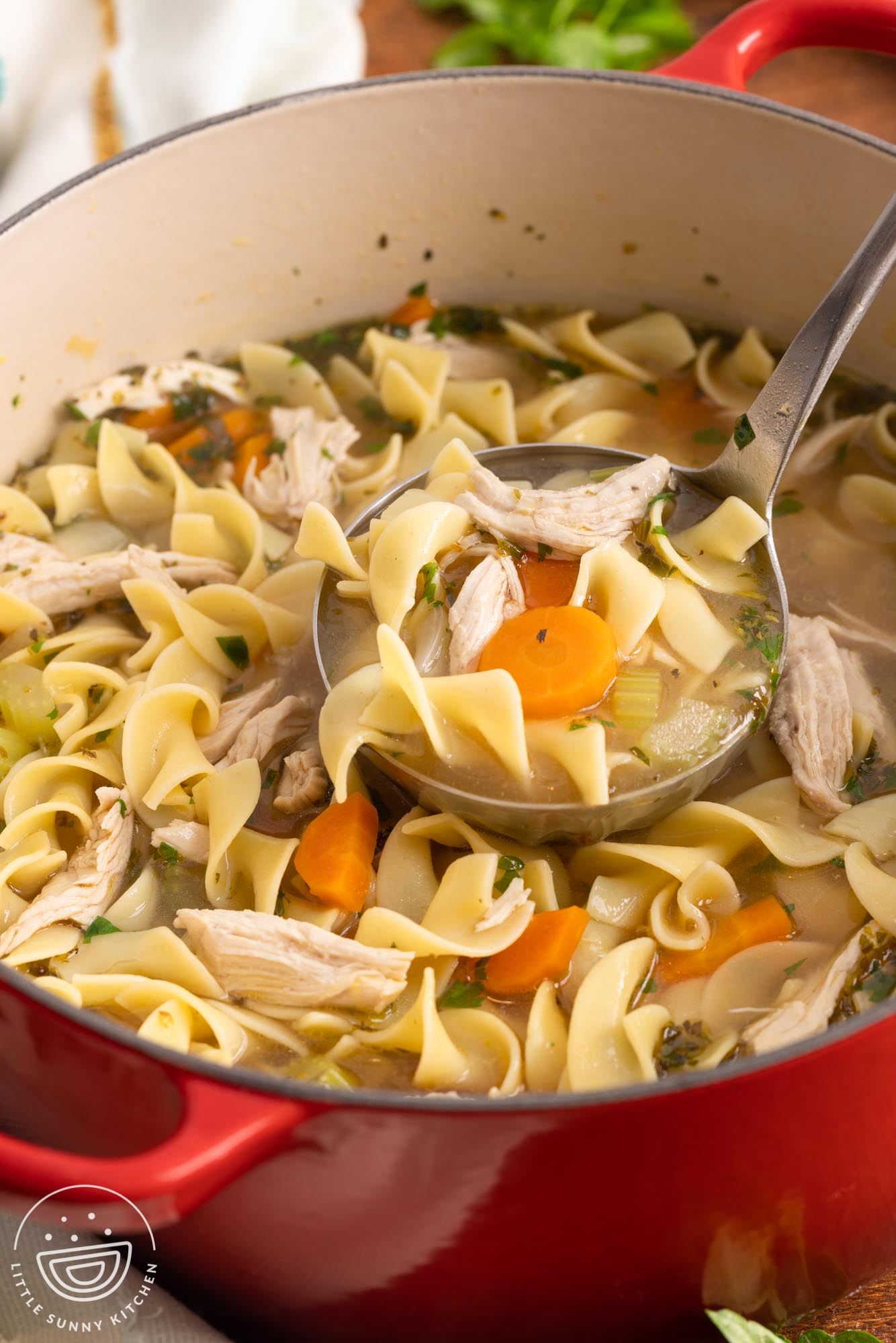 a red dutch oven filled with hearty chicken noodle soup, served with a ladle.