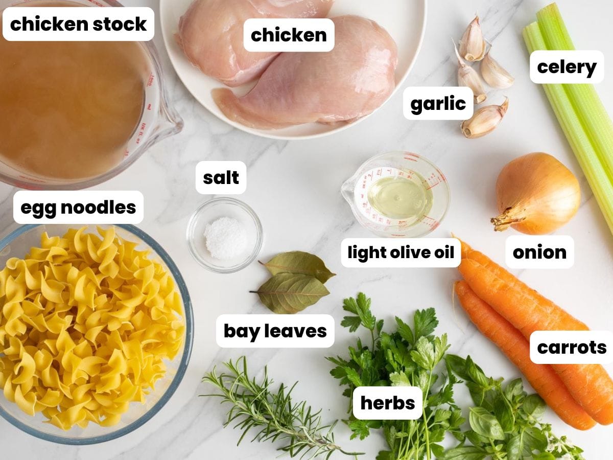 The ingredients for chicken noodle soup, arranged on a marble counter top.