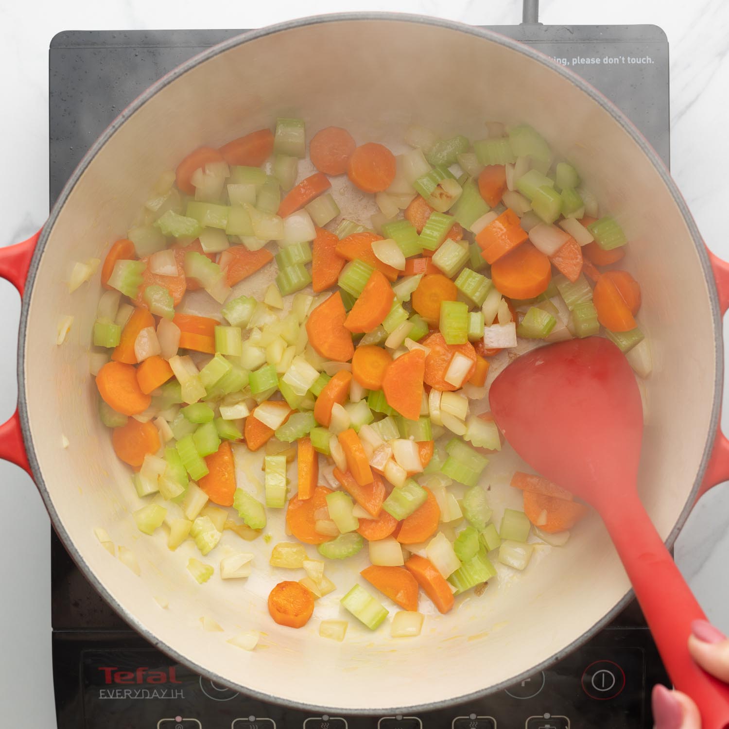 carrots, celery, onions, sauteed in a dutch oven with a red spoon.