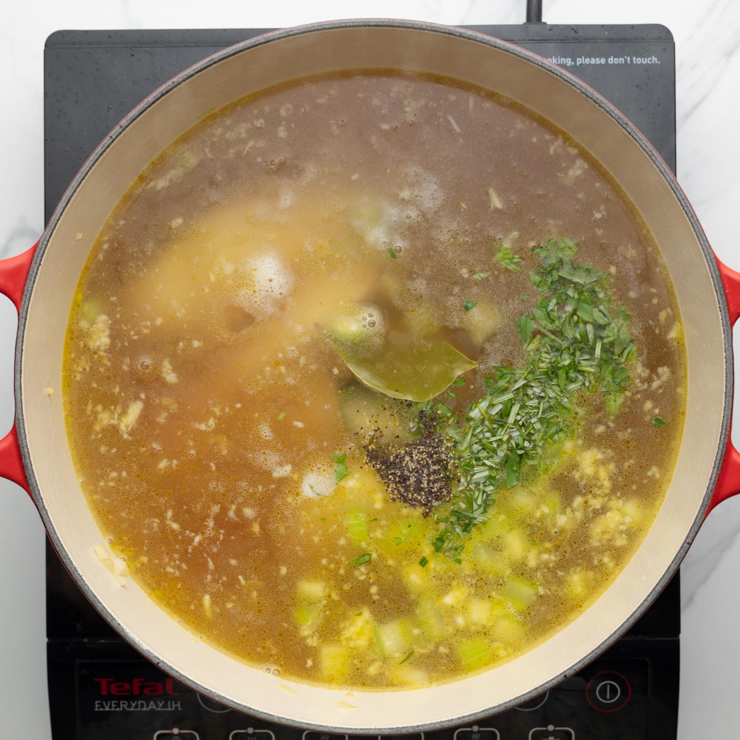 chicken simmering in seasoned broth in a dutch oven.