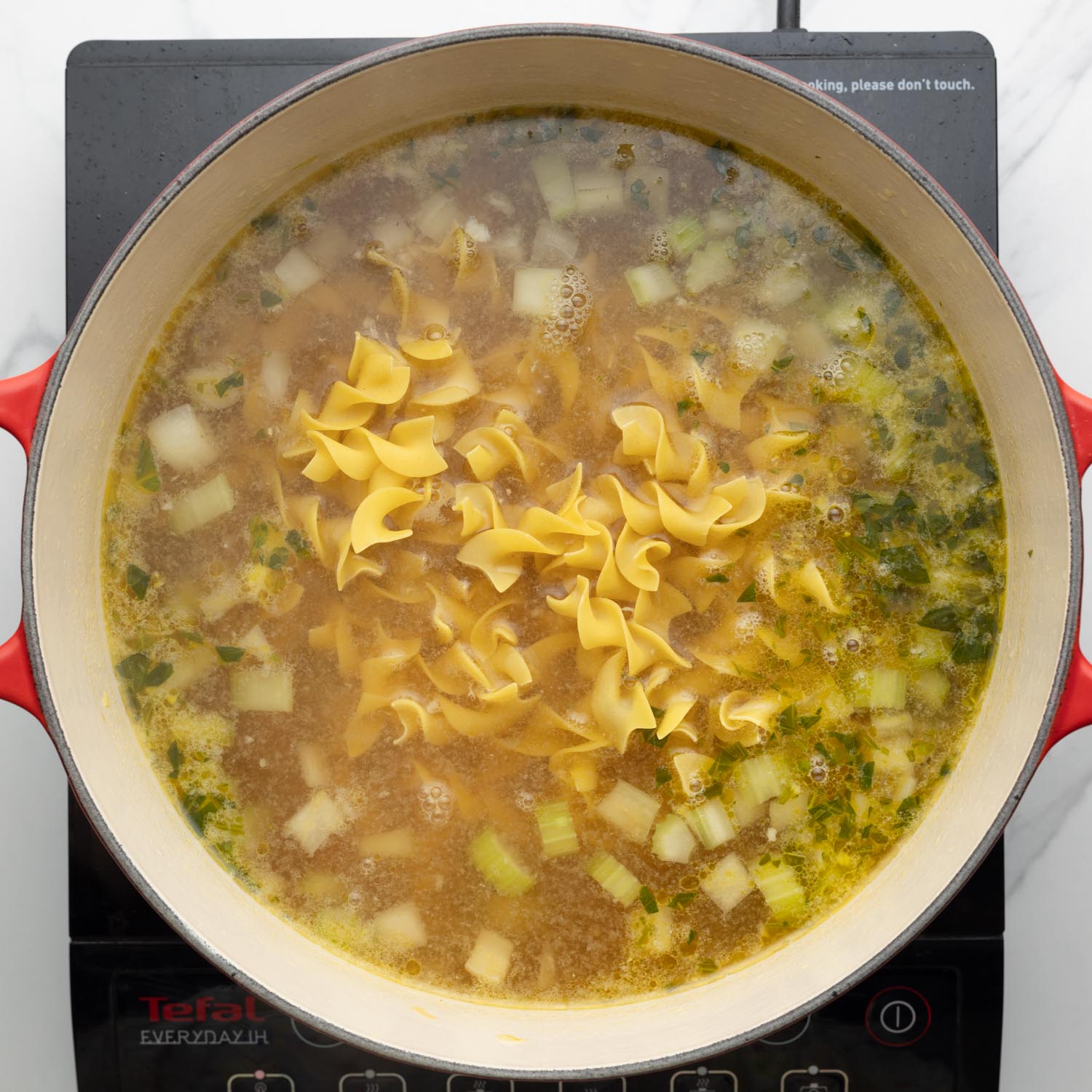 Noodles added to chicken soup in a dutch oven.