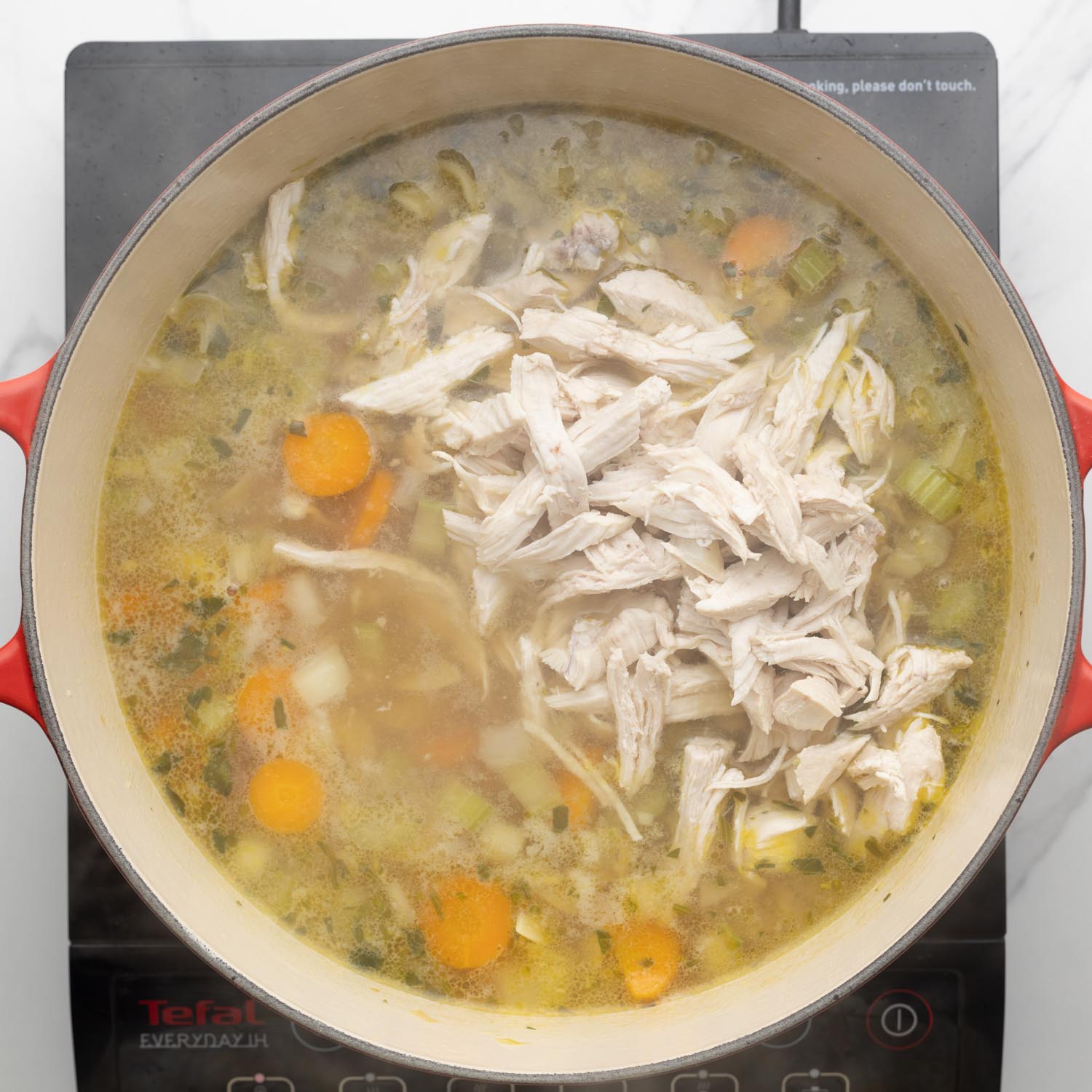 chicken added to a pot of soup over an electric burner.